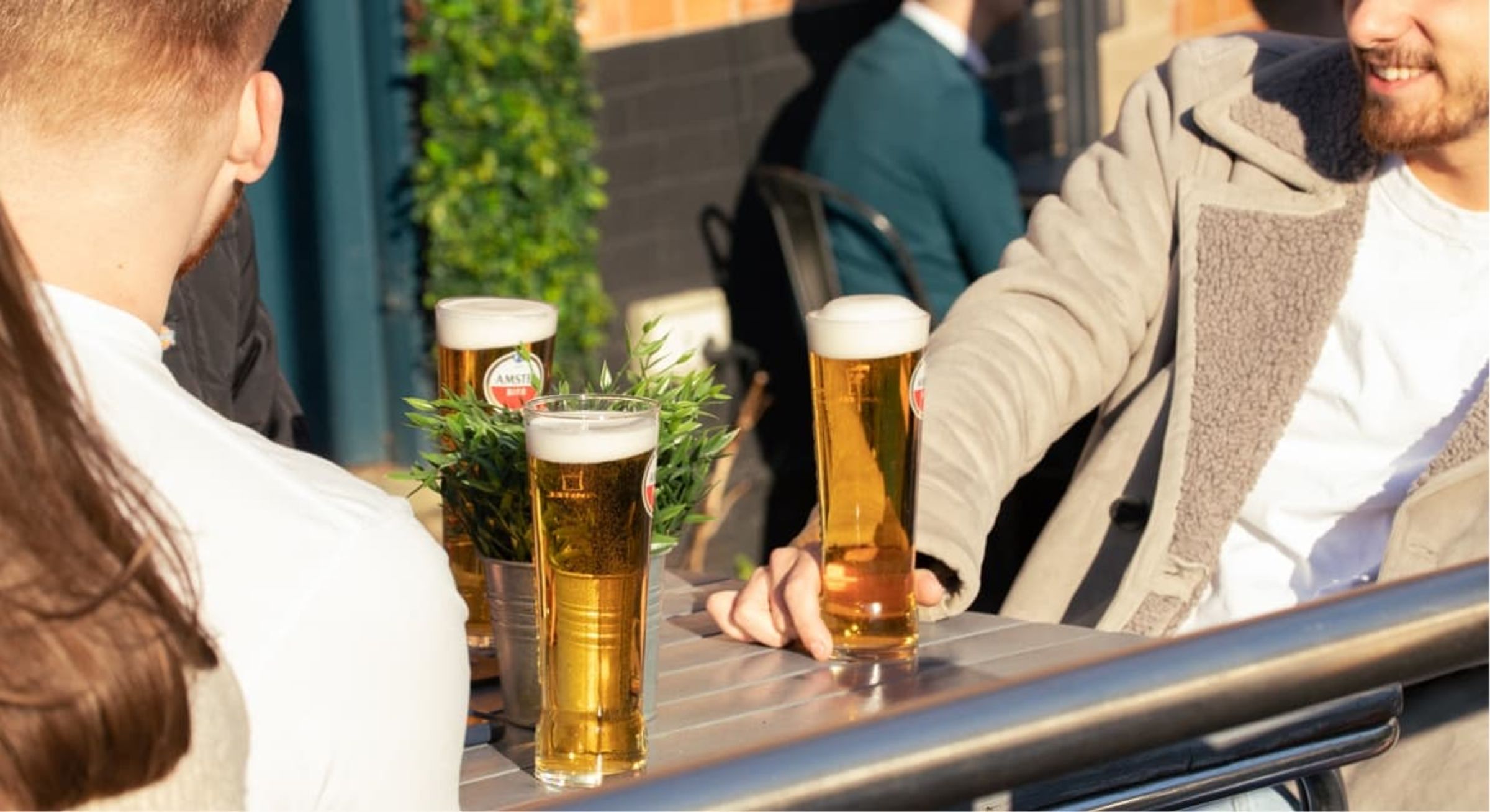 Friends sat on outdoor seating outside a pub with beers on the table