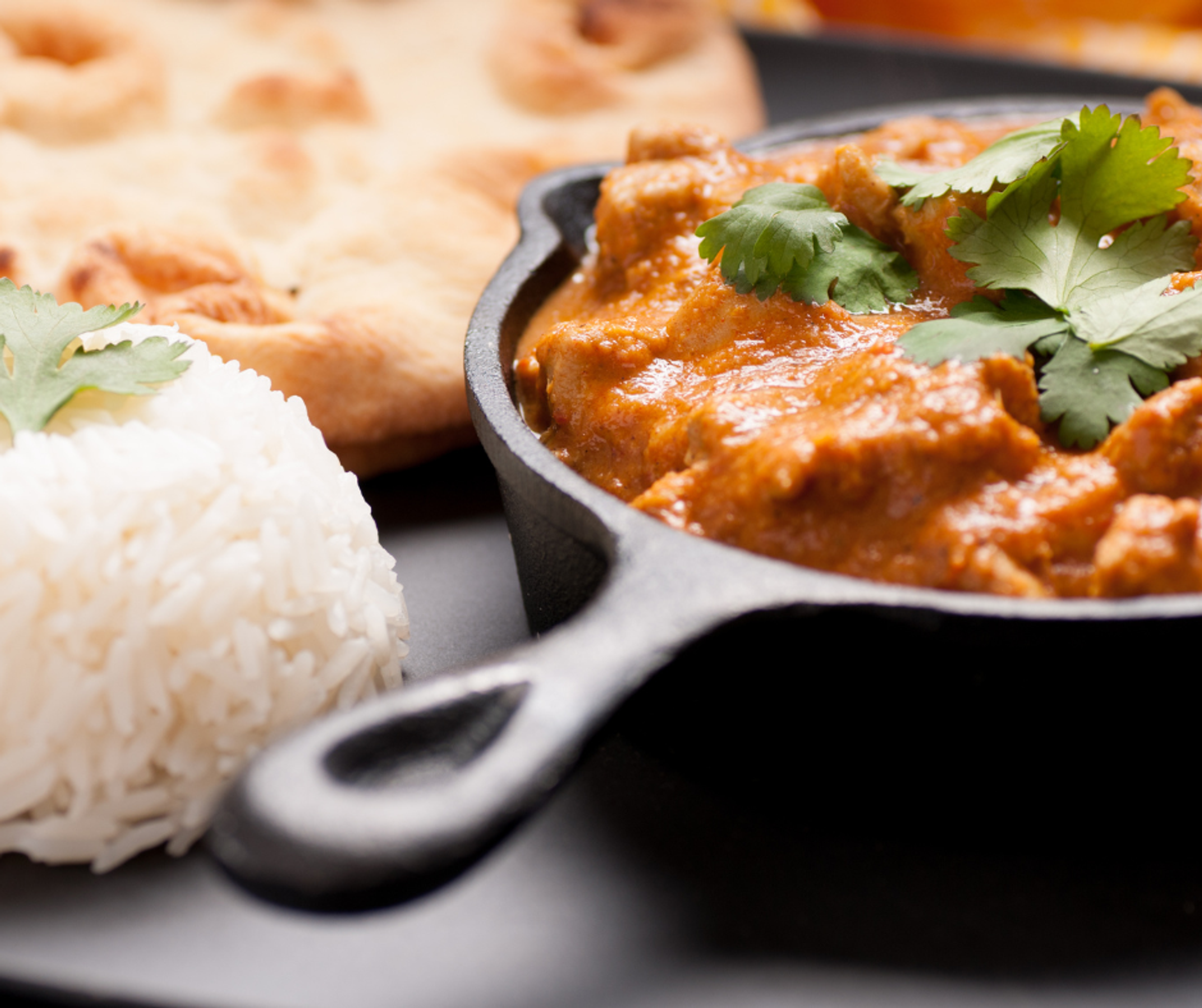 A close up of a curry with coriander, rice and naan bread served on a restaurant plate and mini skillet.