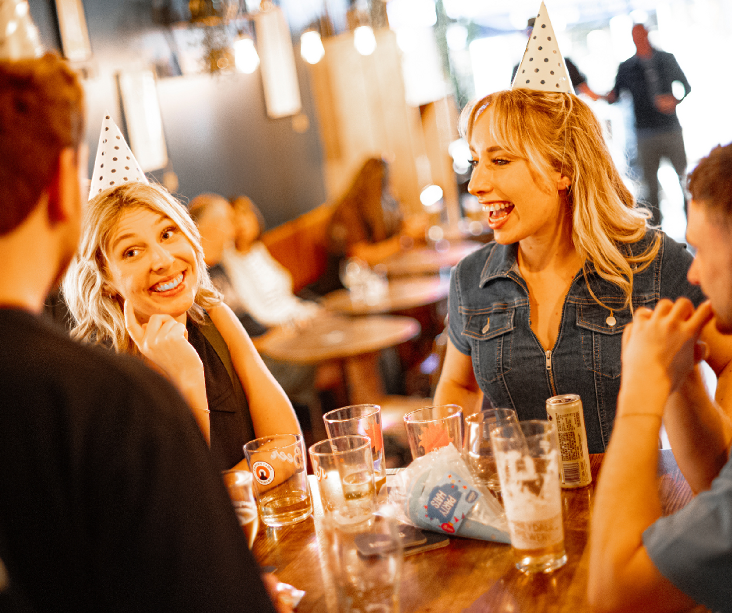 Two women wearing party hats sat at a table with two men and some empty glasses
