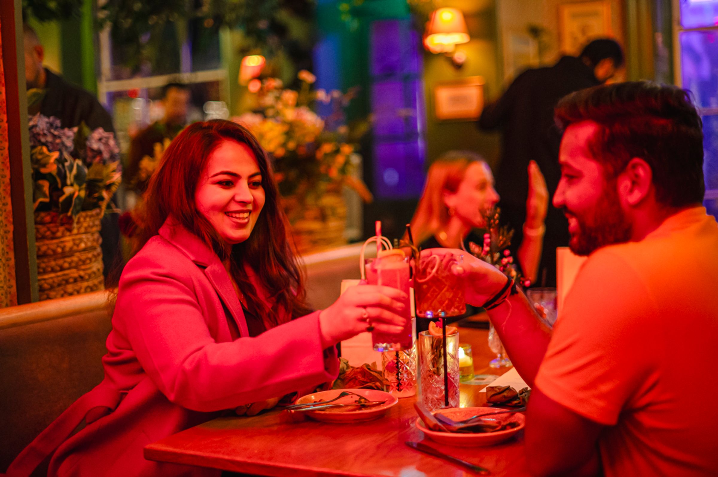 A woman and man at a restaurant table doing cheers with their drinks