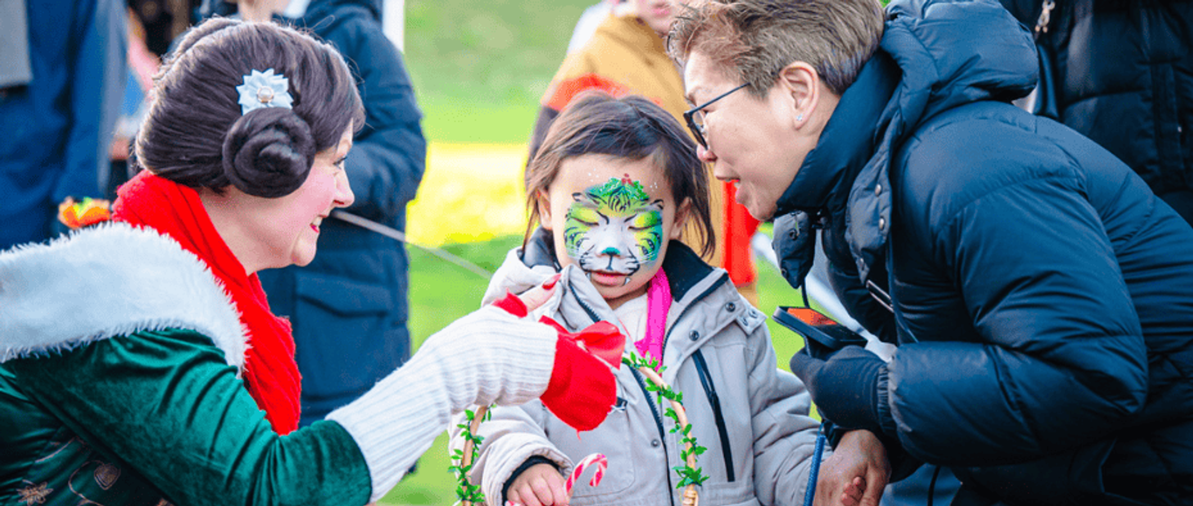 A young child with facepaint alongside her parent and a children's entertainer at the Christmas Market at Nottingham Castle.