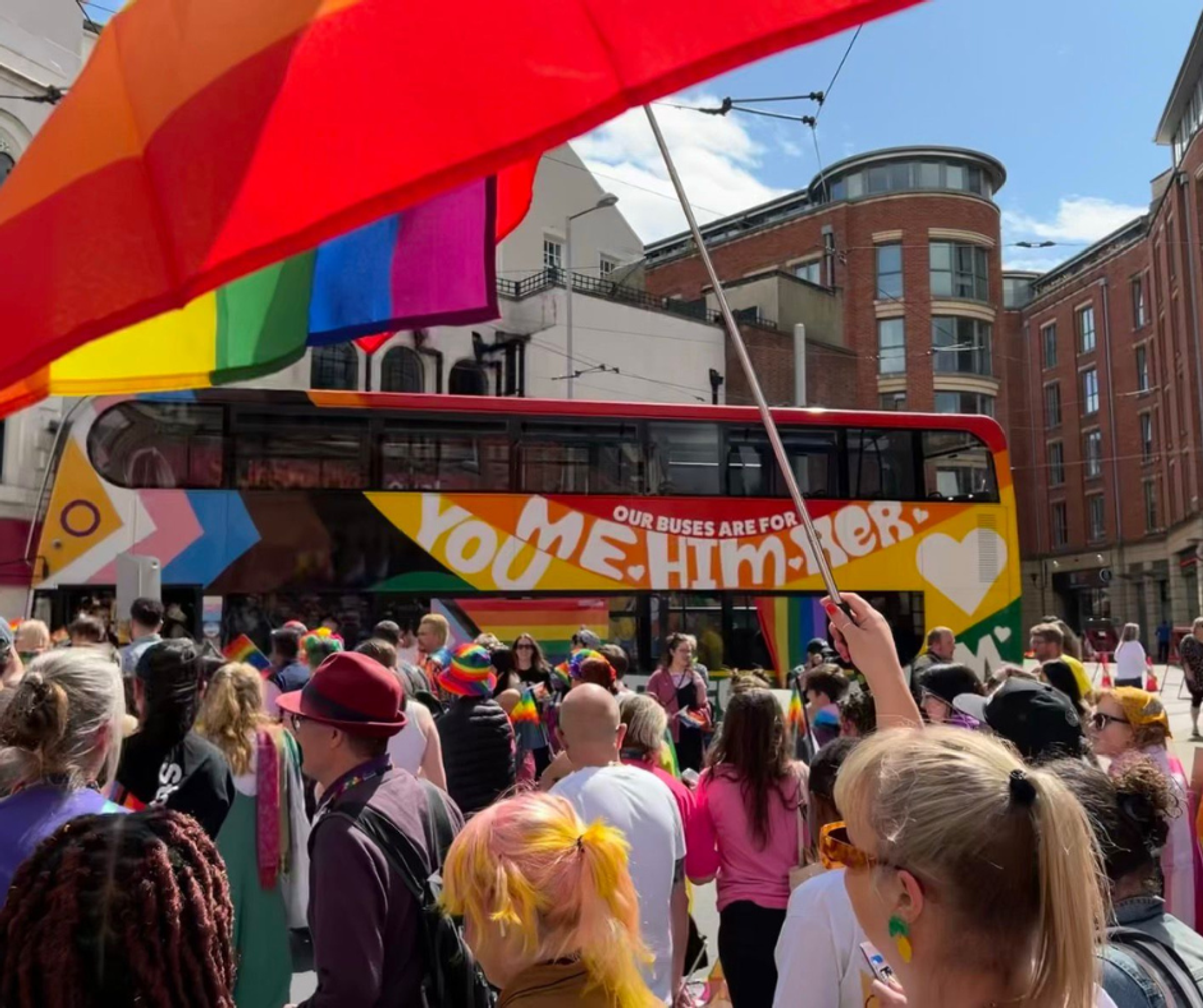 A rainbow painted bus at Notts Pride with a crowd wearing rainbow accessories in front of it
