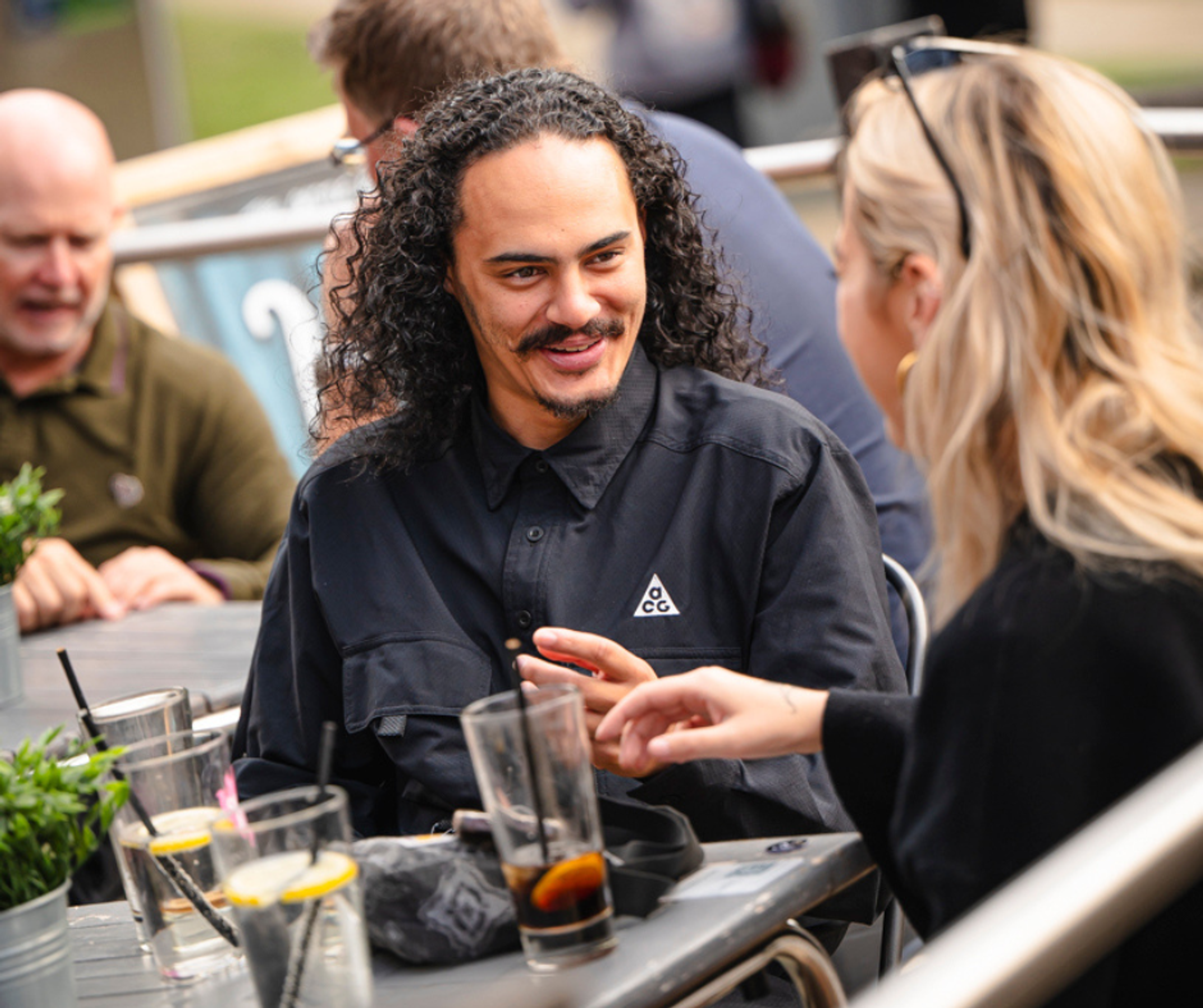 Two people sat at an outdoor restaurant table talking with some drinks