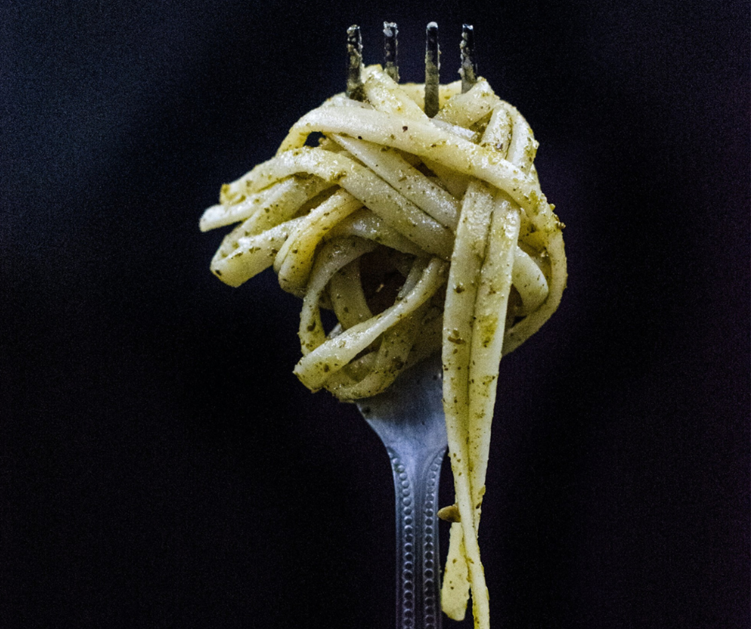 A close up of a fork which holds a twist of spaghetti coated in pesto