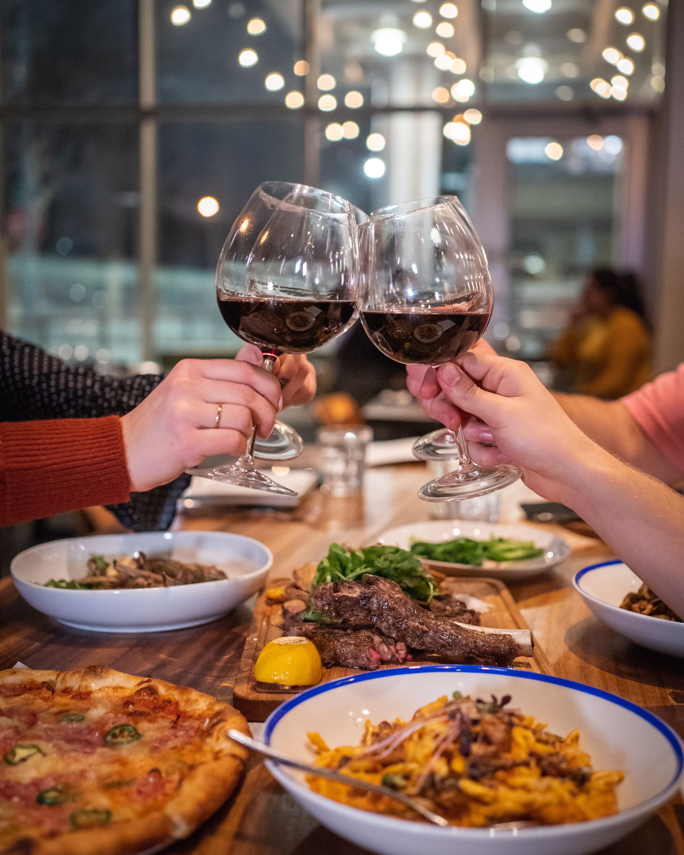 People clinking glasses of red wine over a roast dinner in a restaurant