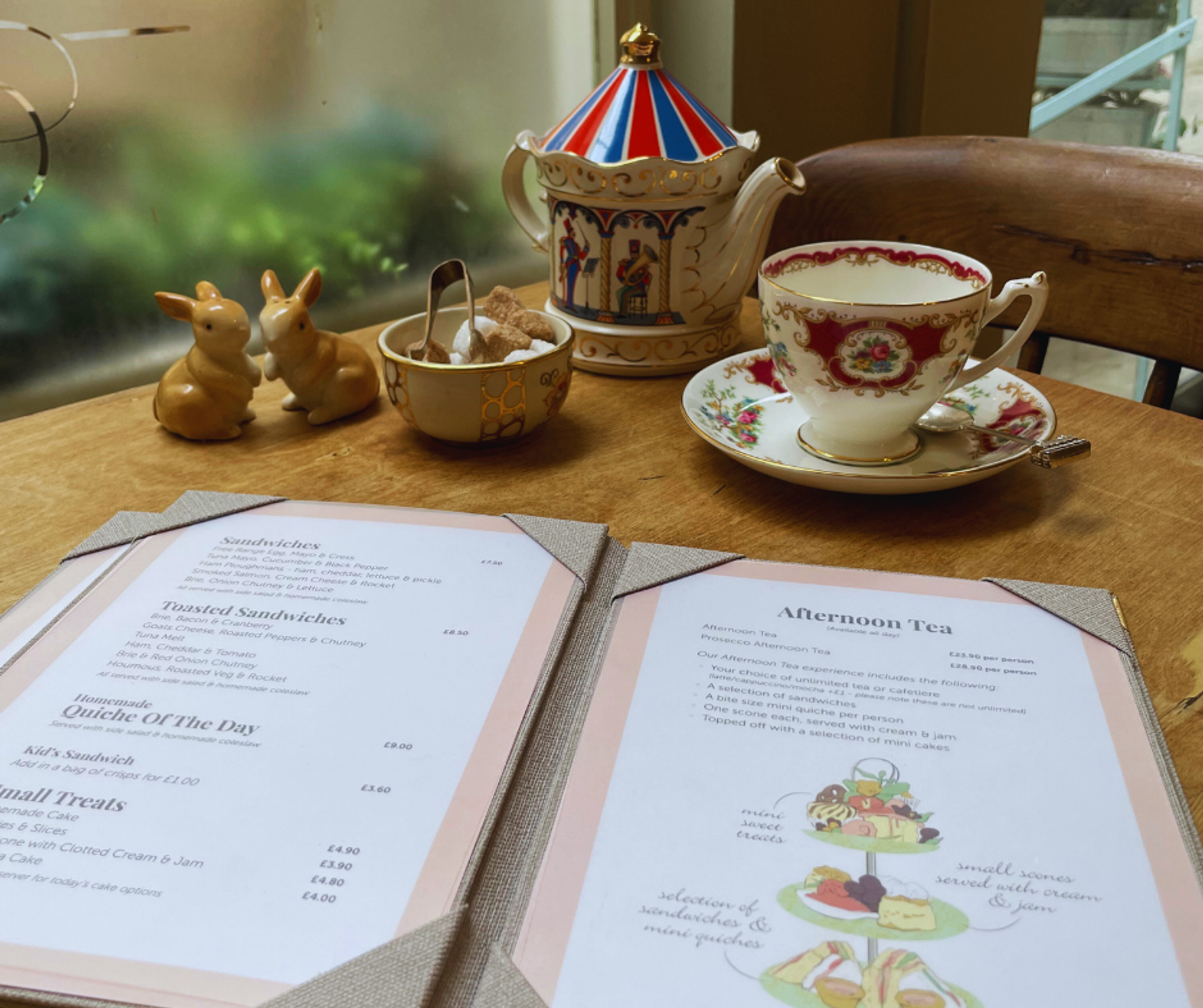 A decorative china cup and tea pot laid on a table in front of a menu for Afternoon Tea