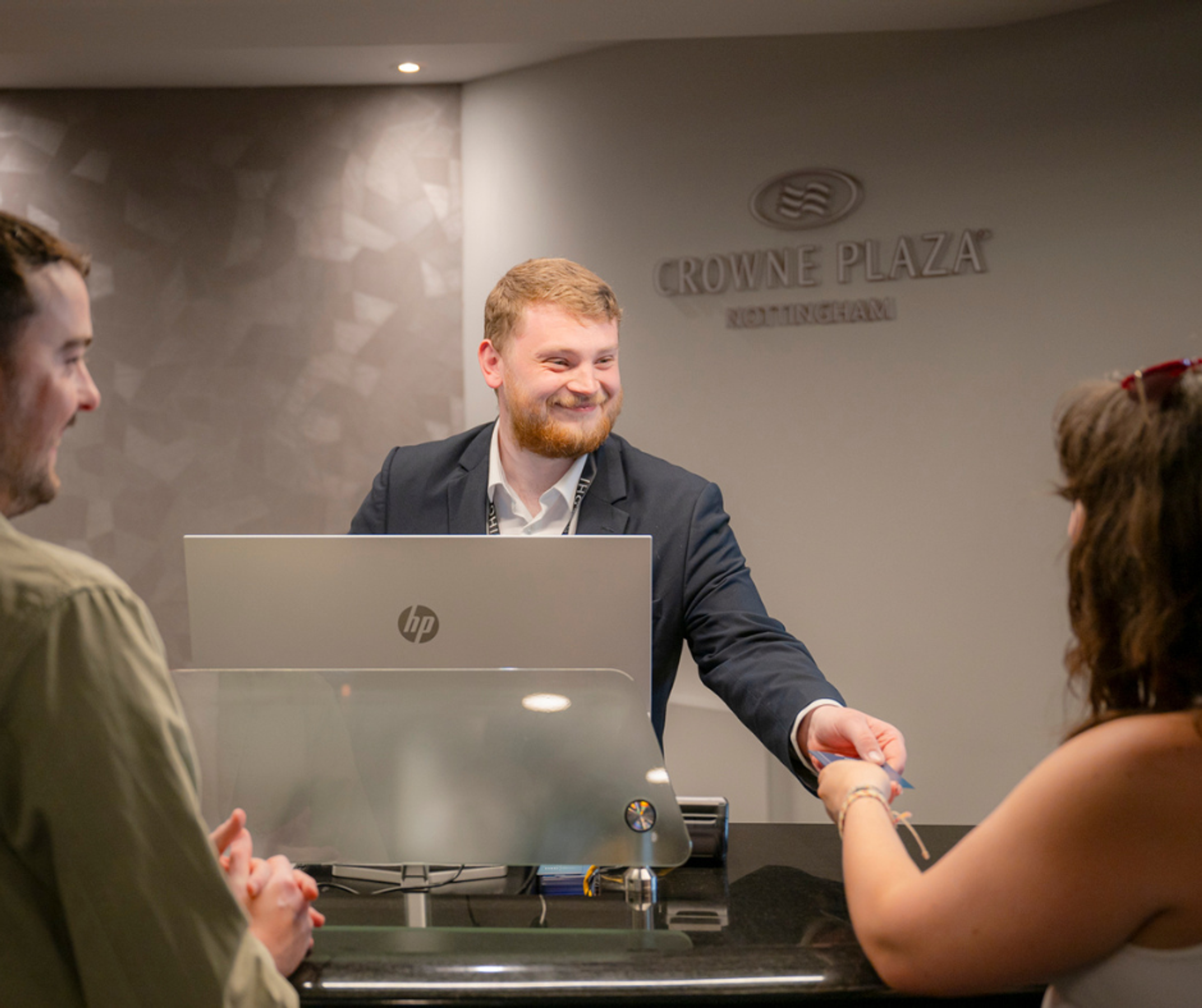 A smiling male concierge hands a room key to a woman at Crowne Plaza Nottingham