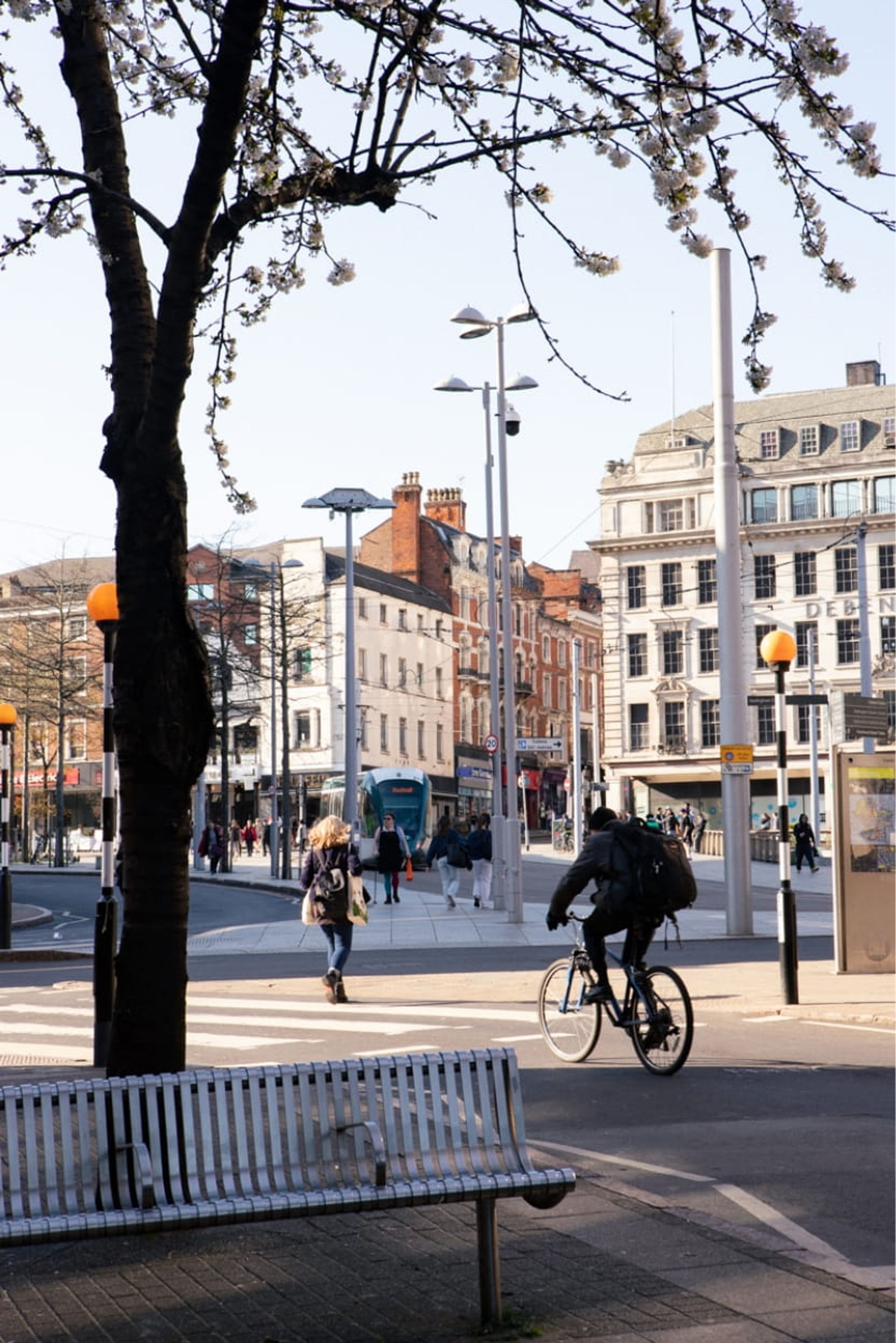A cycling and pedestrians making their way along the edge of Old Market Square, Nottingham with a tram in the background.