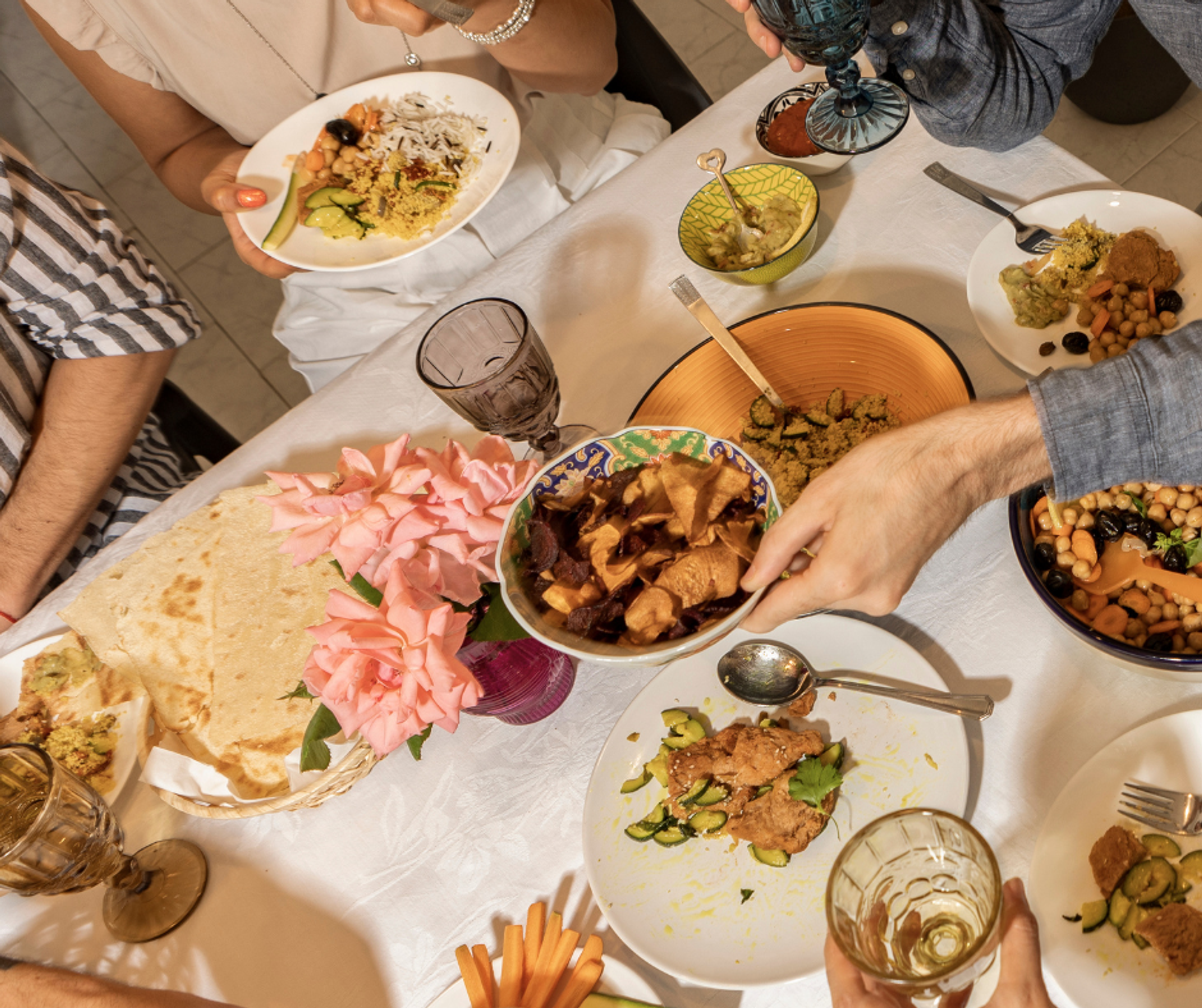 An image of someone passing a plate of food down the table. Around the table we can see several plates of food and the hands of some diners.