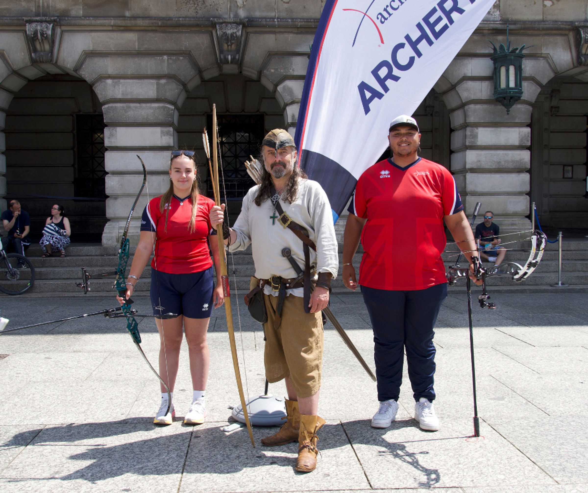Two young GB archers along with Nottingham's Robin Hood in costume, stood with bow and arrows in Nottingham's Old Market Square