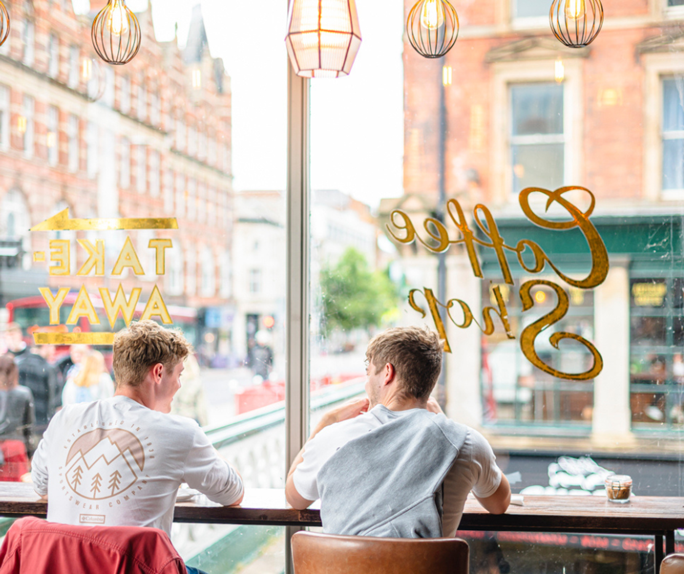 Two men sat in the window seat of a coffee shop near Nottingham Railway Station, looking out over the river and architecture