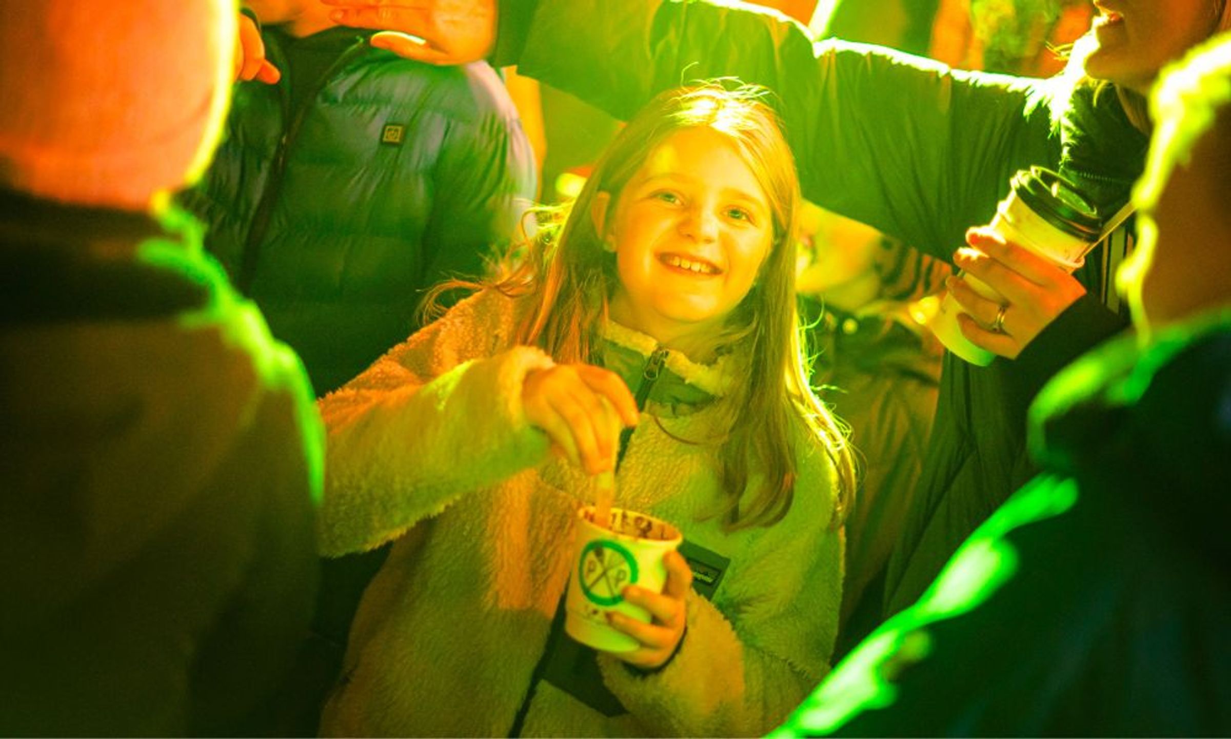 A young girl at a winter outdoor event eating street food from a cup.
