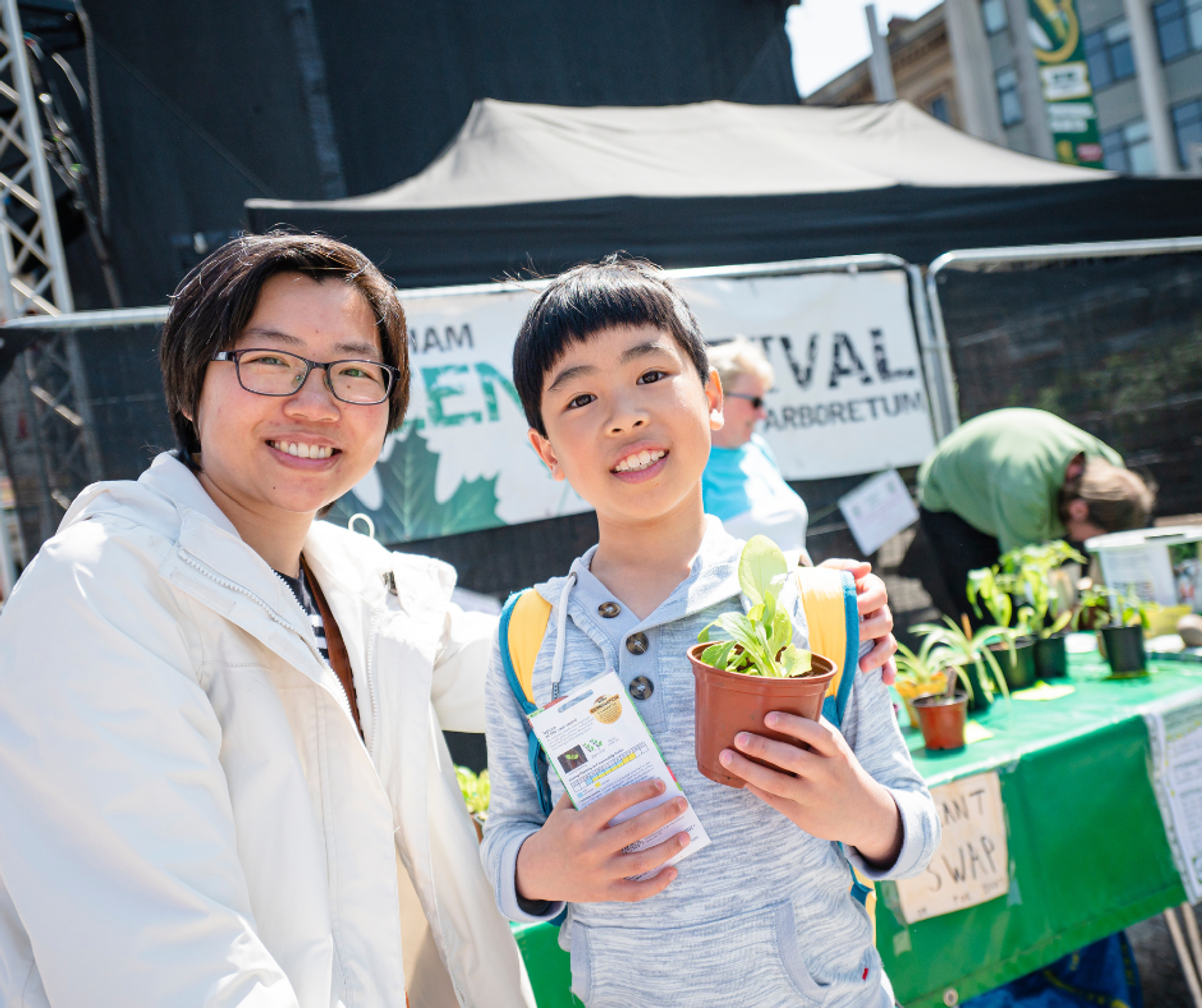 A woman and young boy smiling with the boy holding up a plant and some seeds during Nottingham's Green Hustle festival