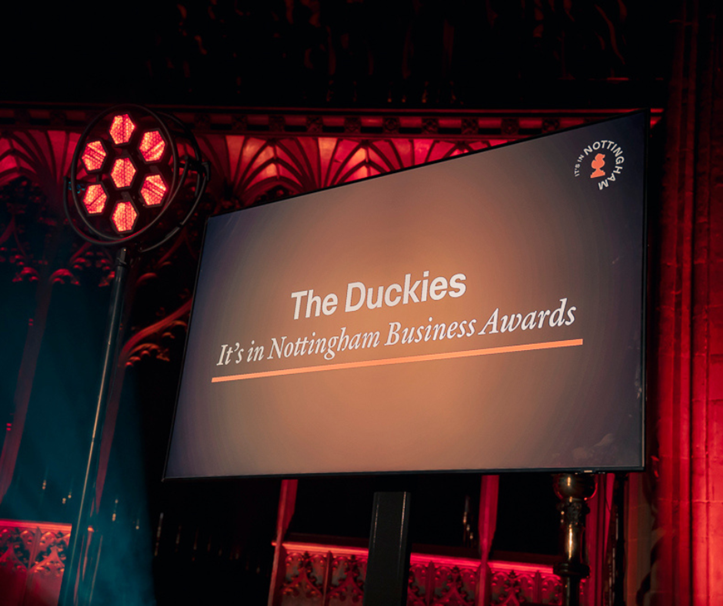 A large screen reading "The Duckies: It's in Nottingham Business Awards" The screen is displayed in a church, with red lighting and architecture visible in the background.
