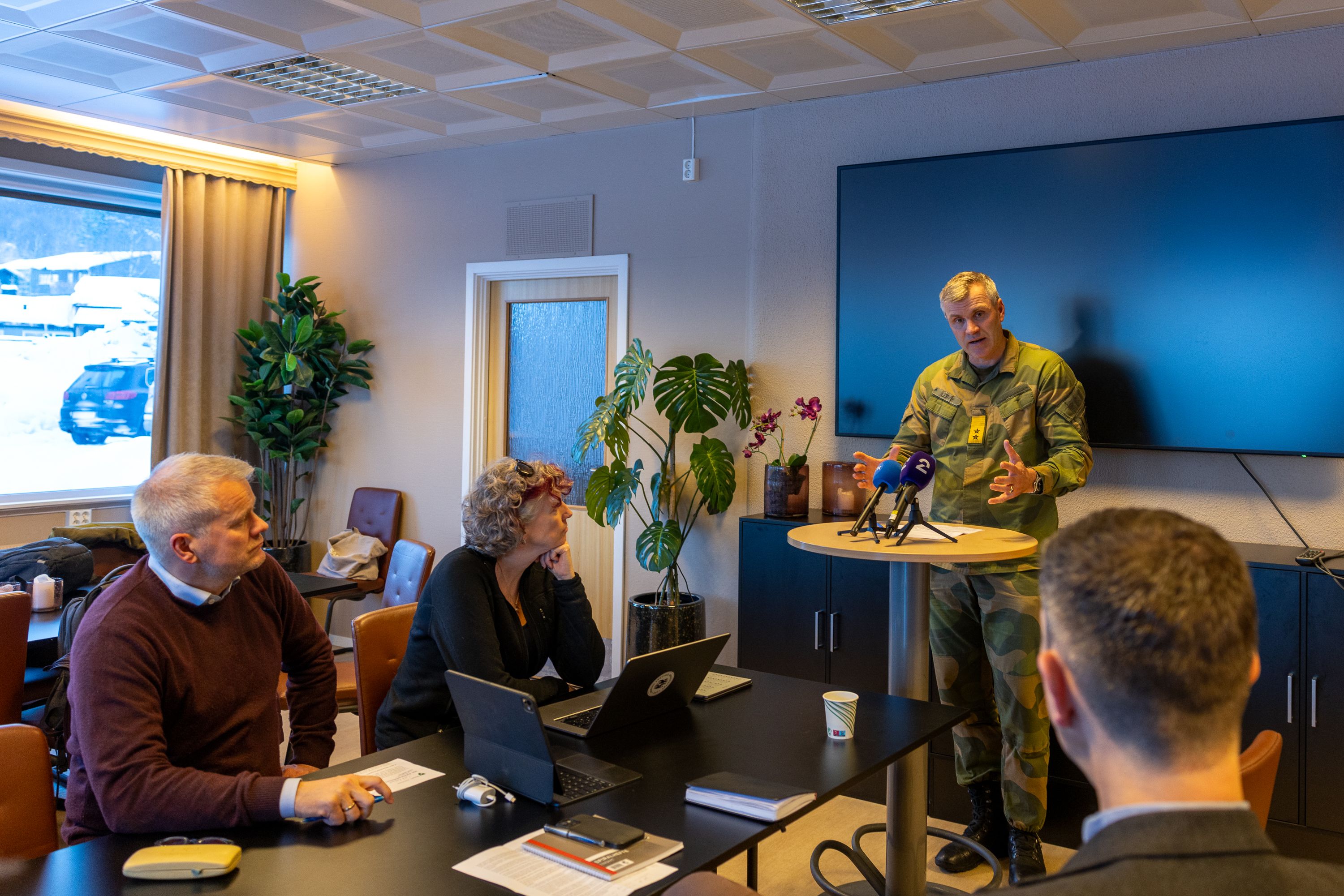 Mann i uniform som snakker til tre sivilister 