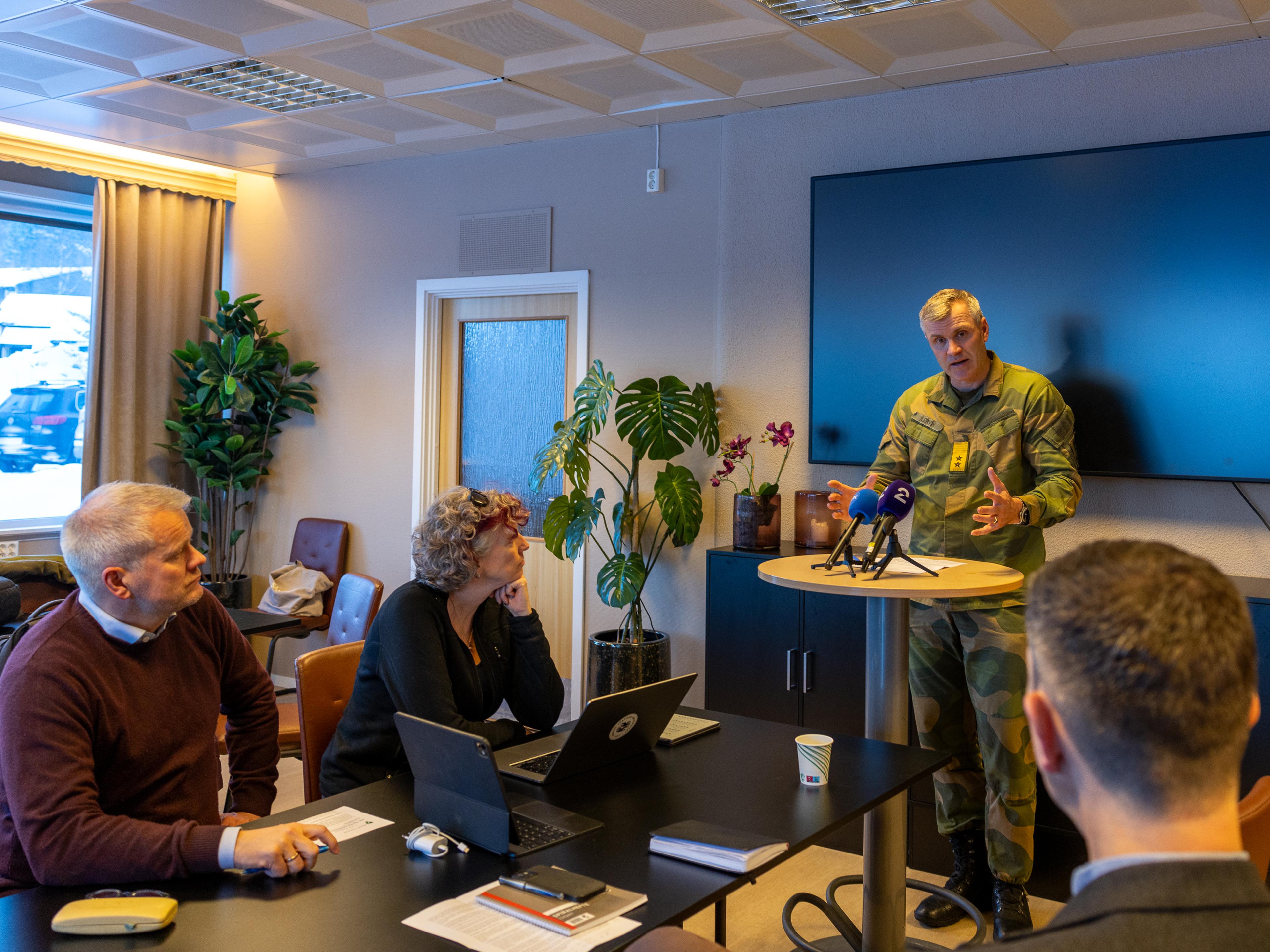 Mann i uniform som snakker til tre sivilister