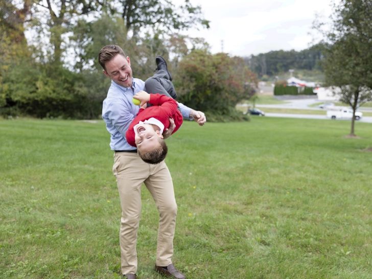 Ein Mann hält einen Jungen seitlich in seinen Armen, während der Junge lacht