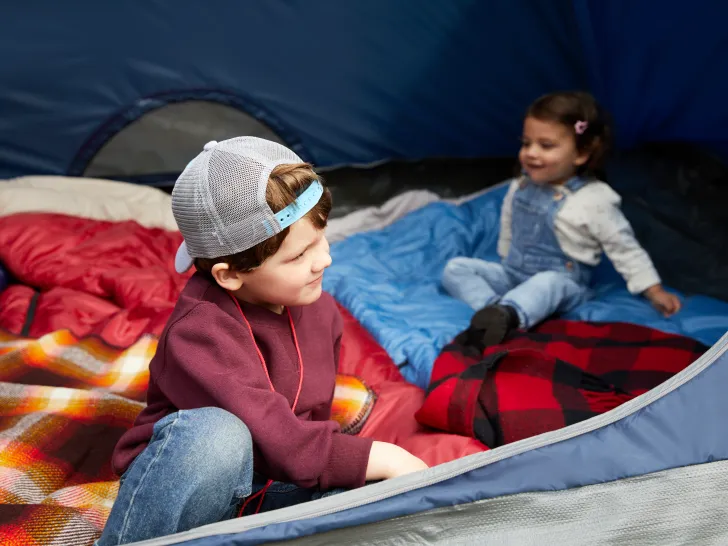 A young boy and girl sat on sleeping bags inside a tent.