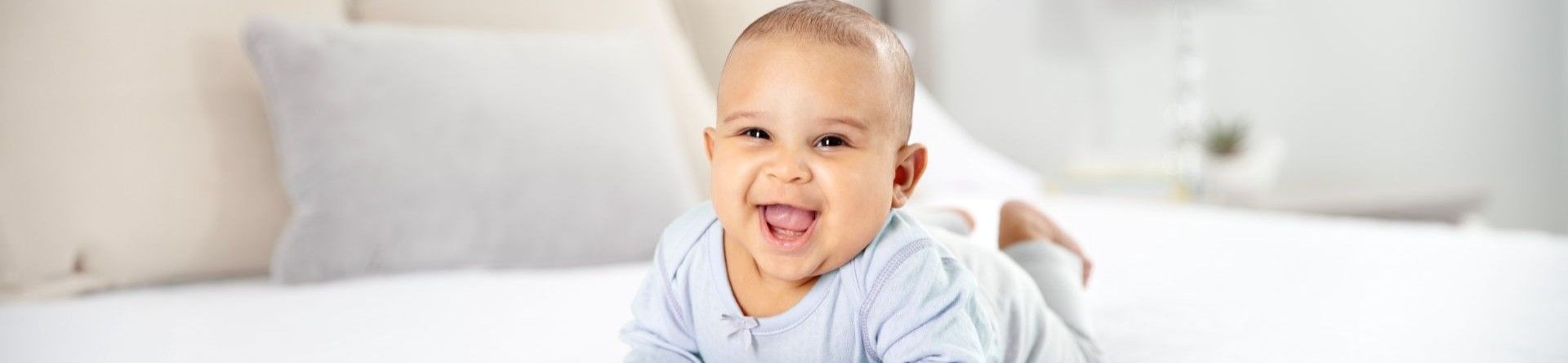 A baby lying on his stomach, leaning on his arms with a big wide smile.