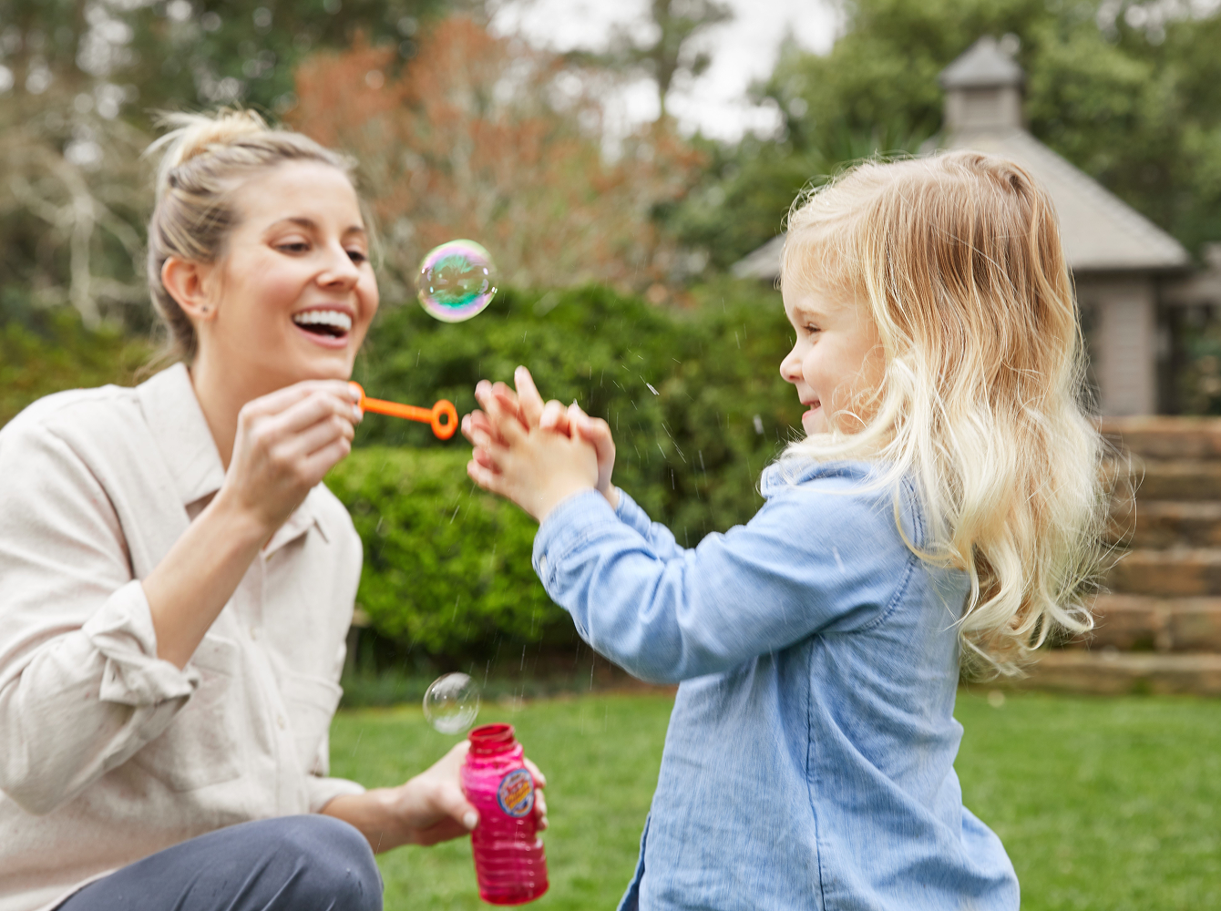 A woman and a little girl joyfully playing with bubbles in a park.