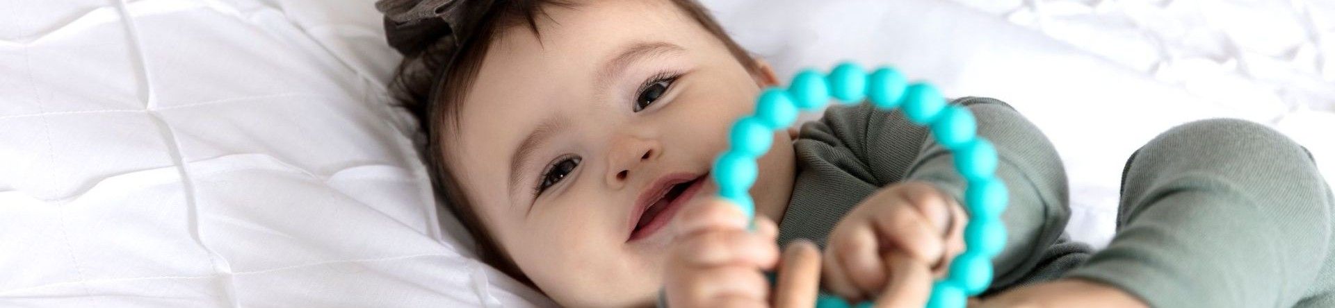 A young baby lying on a bed looking at the camera holding a small toy with both hands.