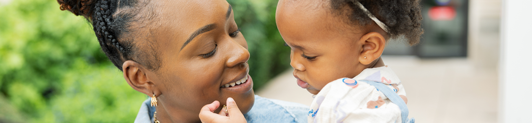 A mother holding her daughter while the little girl plays with her mother’s necklace.