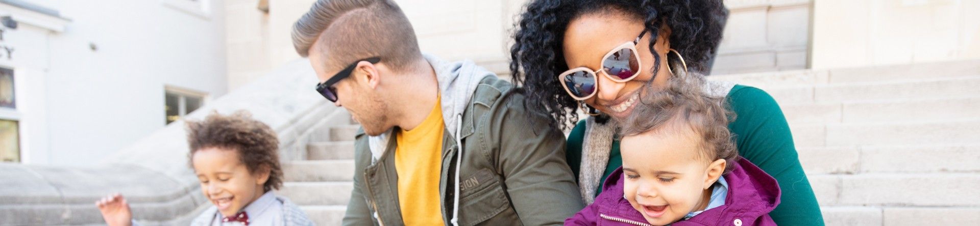 A man and woman sat outside on some steps with a small boy sat next to the man and a little girl sat on the woman's lap.