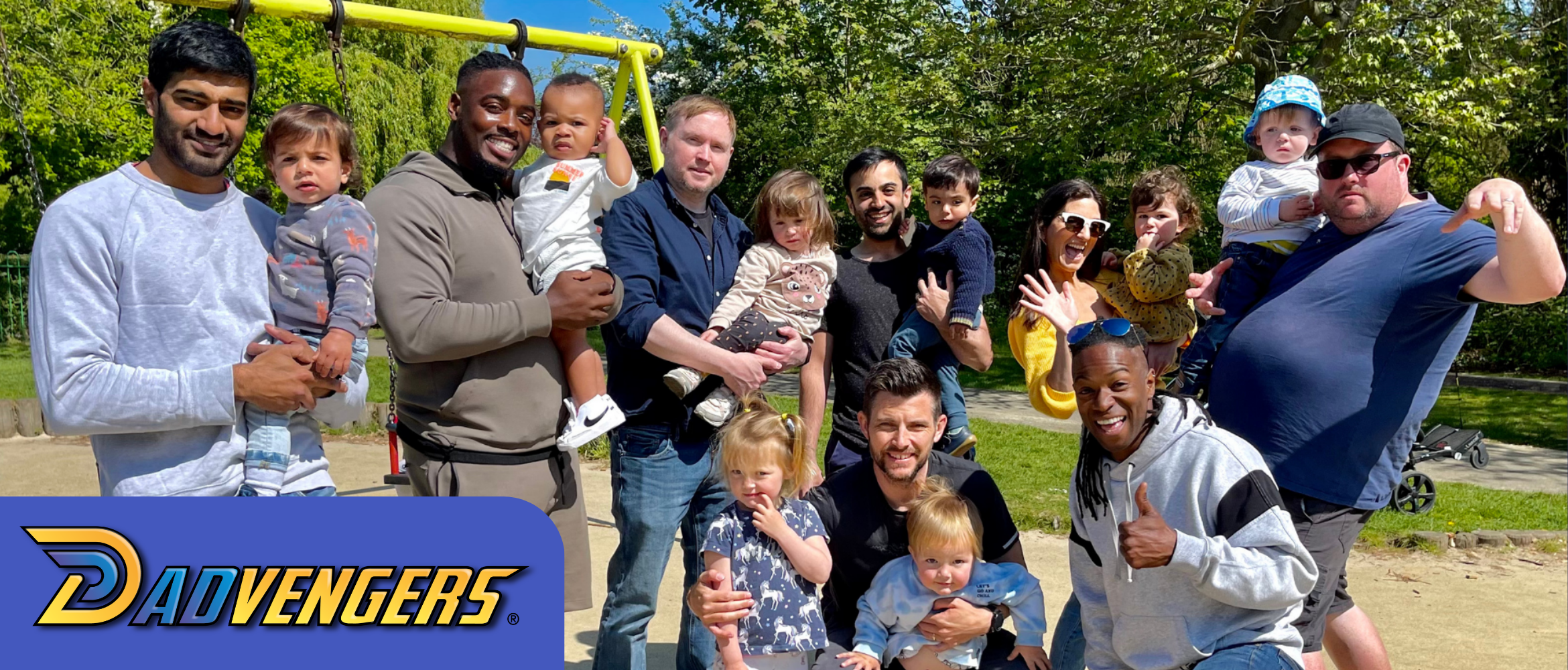 A group of Dads at a playground holding with their kids in a sand pit, with the word Dadvengers in the bottom left corner.