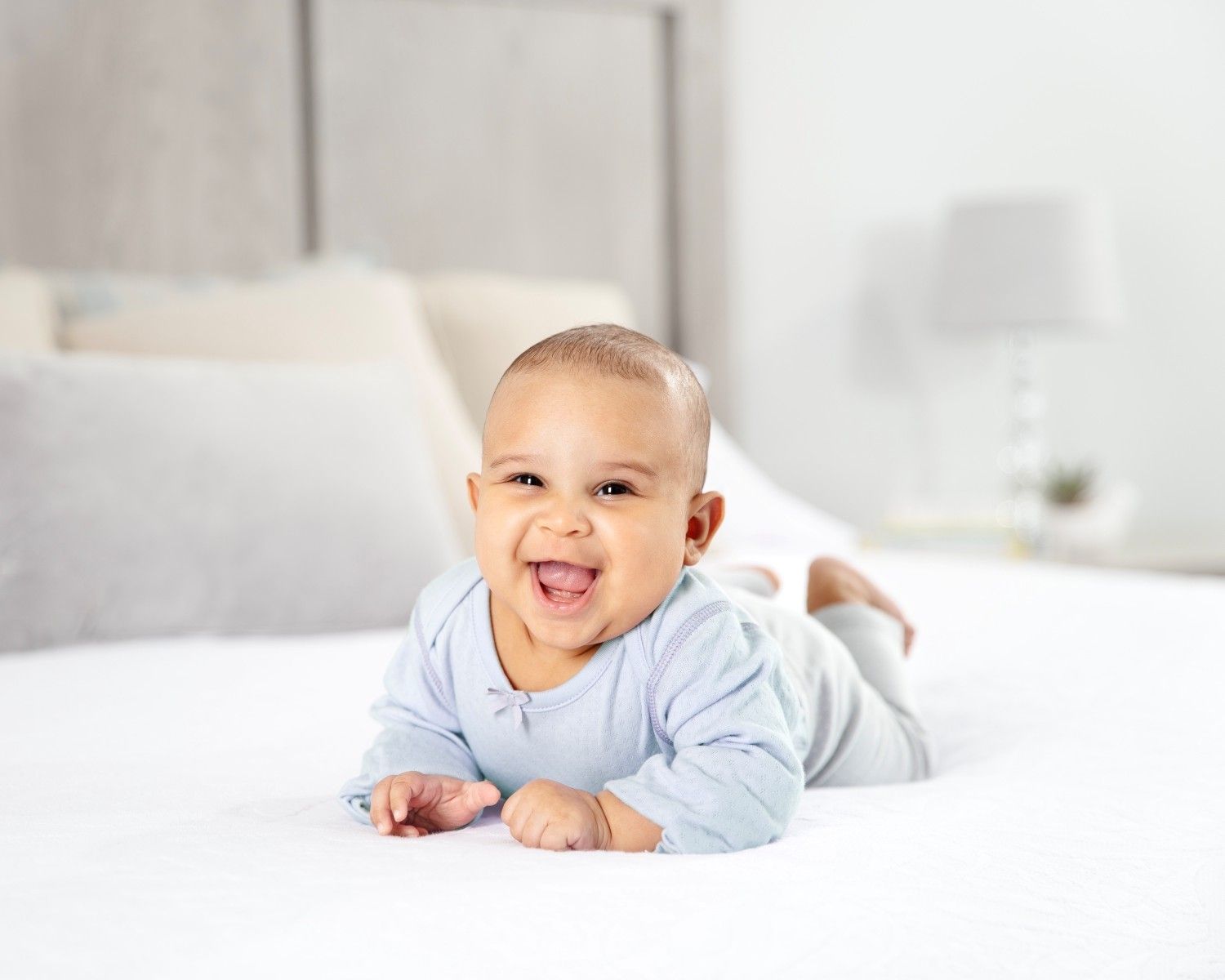 A baby lying on his stomach, leaning on his arms with a big wide smile.