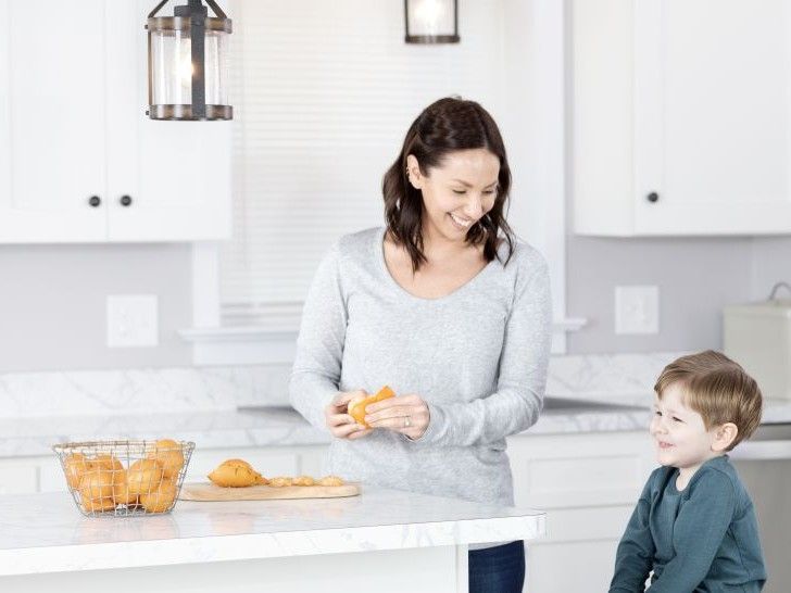 Eine Frau schält in der Küche eine Orange; neben ihr sitzt ein Junge.