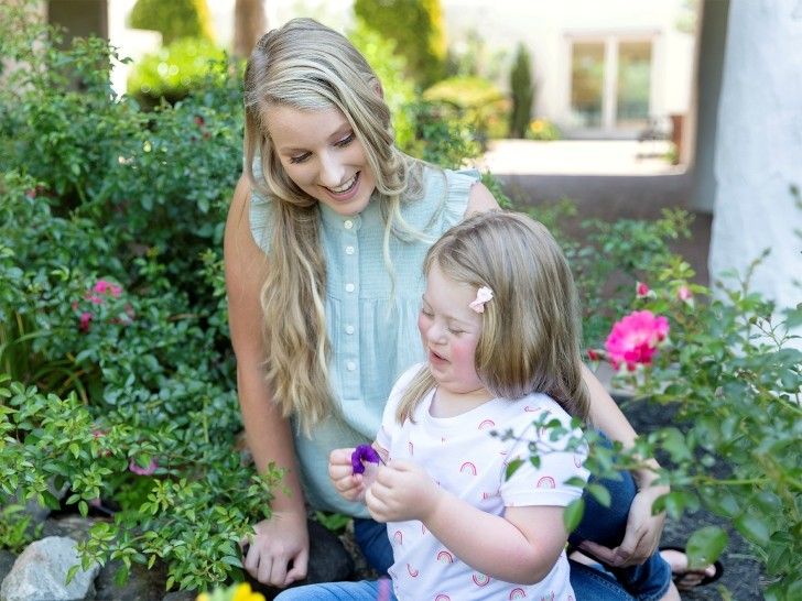 A woman and a girl sat in the garden, with the girl holding a purple flower.