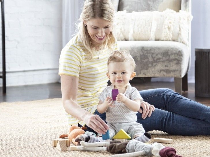 Eine Frau sitzt auf dem Boden, während ein kleiner Junge vor ihr spielt.