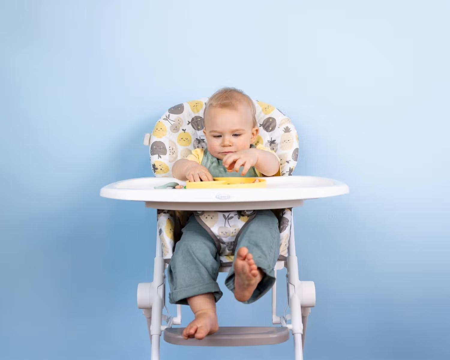 Un jeune garçon assis dans une chaise haute regarde la nourriture sur le plateau et la saisit avec les deux mains.