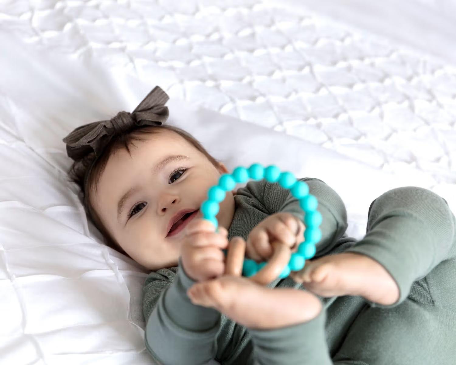 Un neonato sdraiato su un letto guarda la fotocamera tenendo un piccolo giocattolo con entrambe le mani.