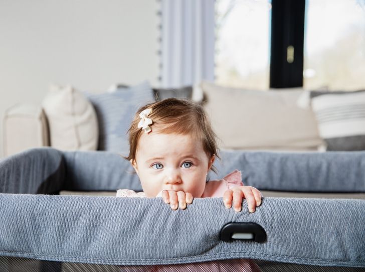 Ein Kleinkind im Reisebett, das sich am Rand festhält