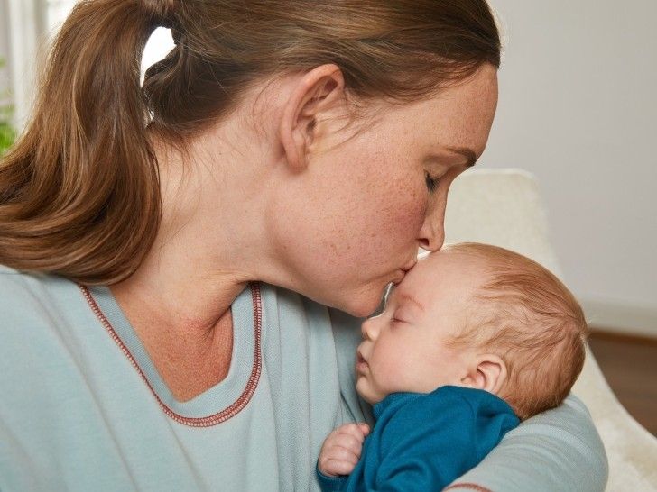 A mum holding a small baby in her arms while gently kissing his forehead.