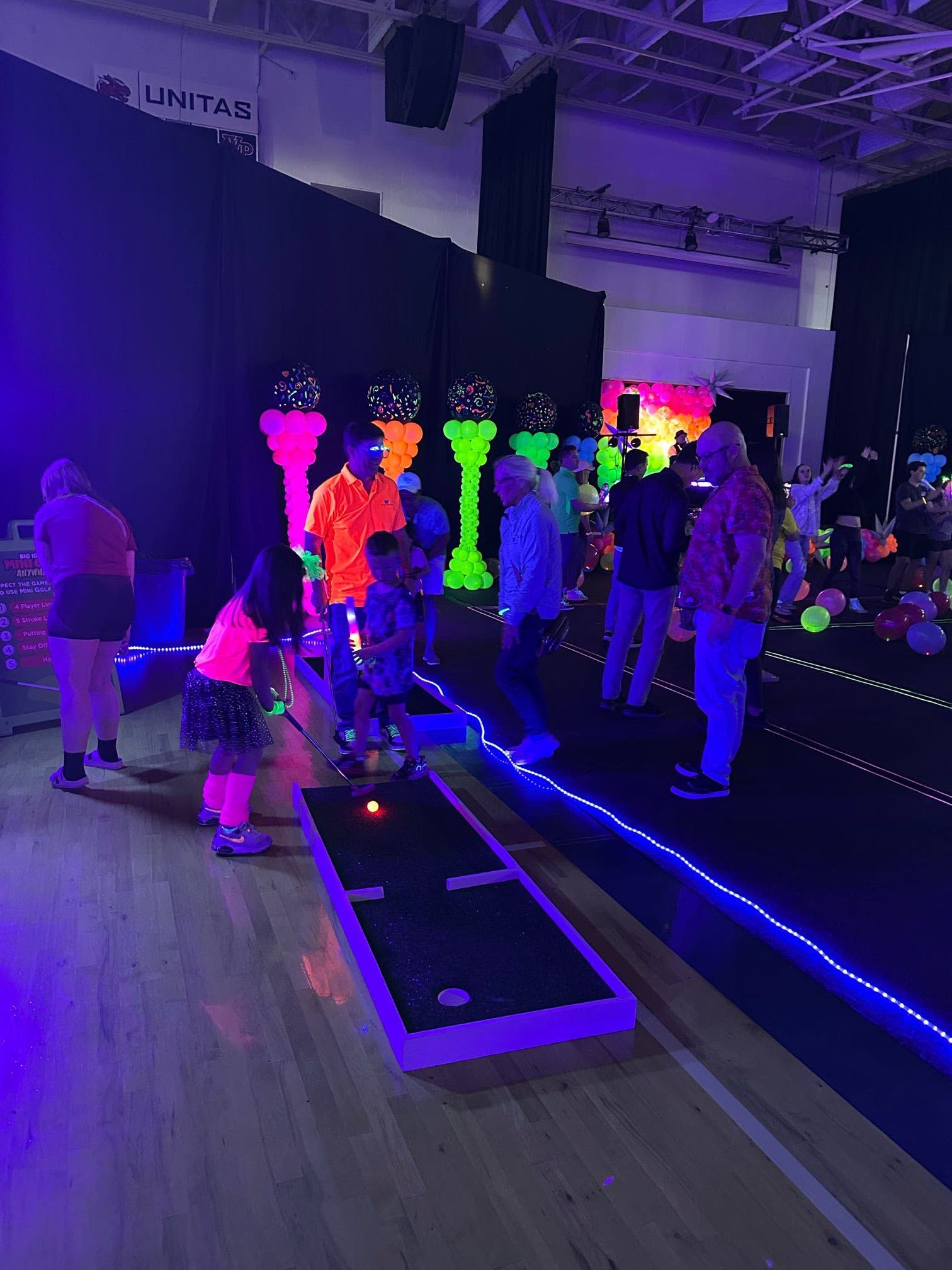 a glowing mini golf lane and neon obstacles set up in a darkened hall