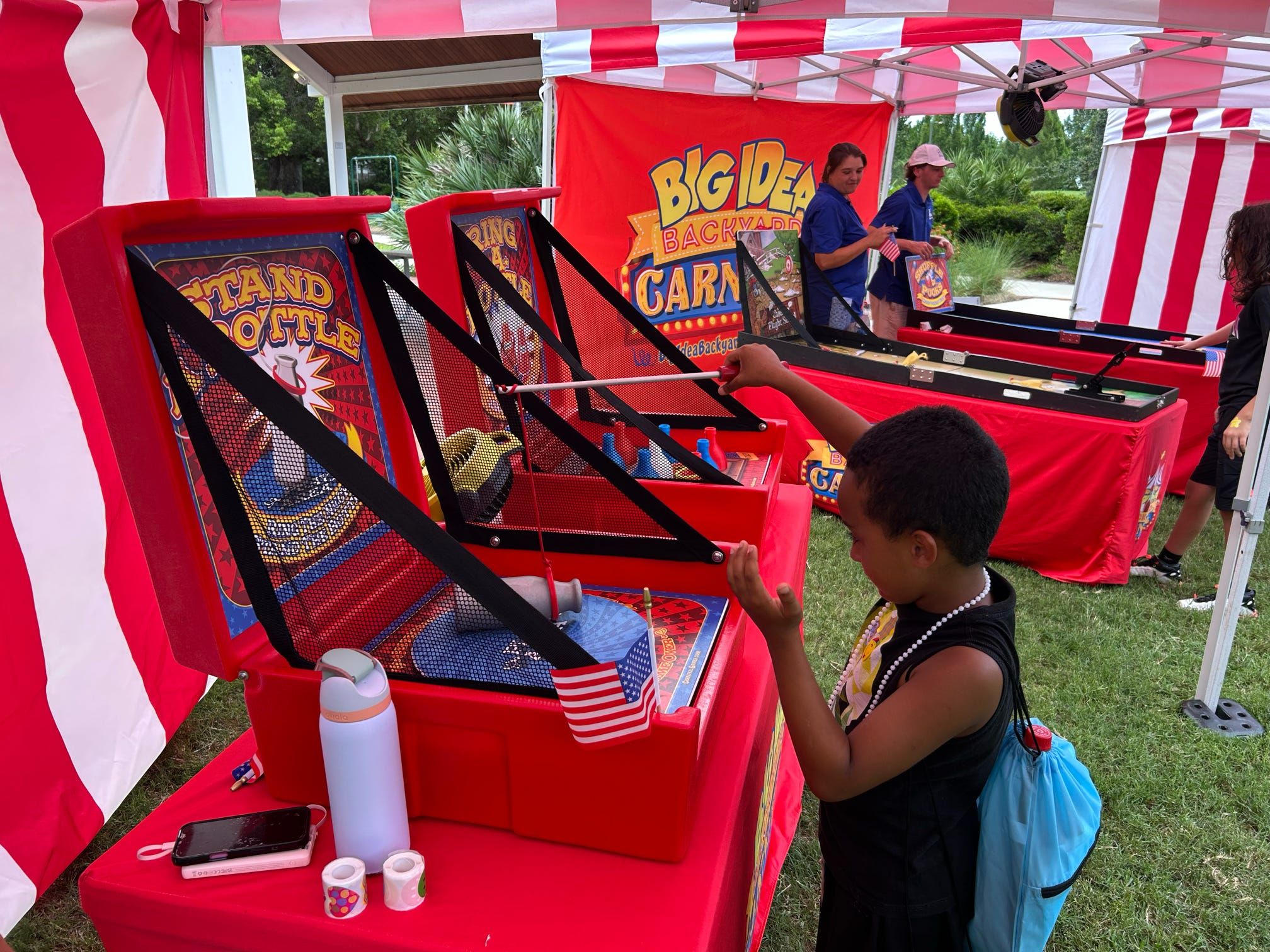 Kids playing stand the bottle under a red and white striped tent at a carnival party