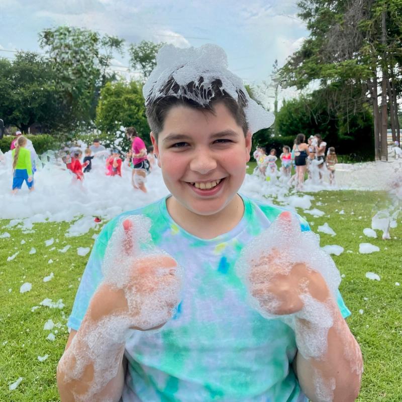 Kid smiling and thumbs up at a field day foam party.