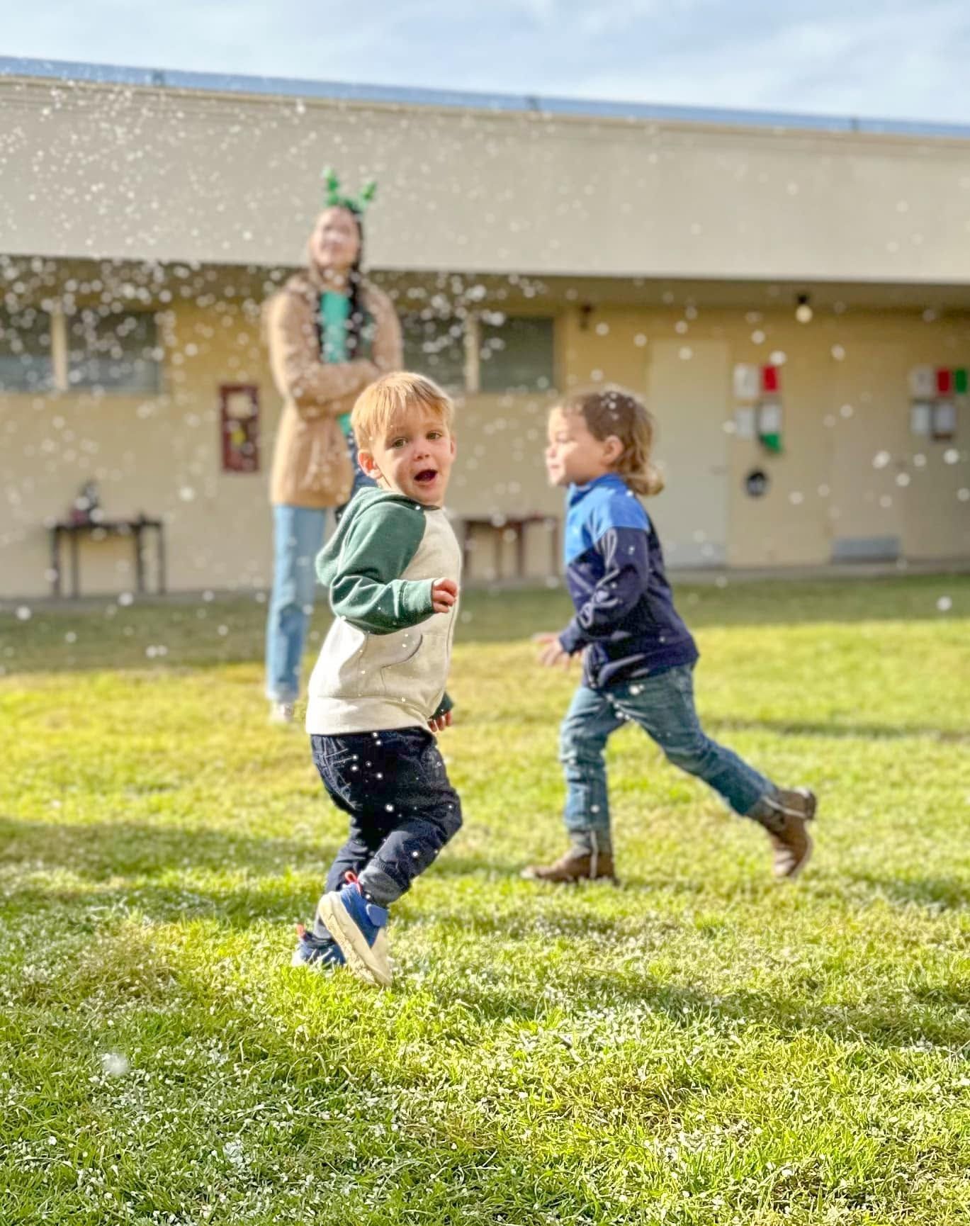 Two toddlers run through falling snow