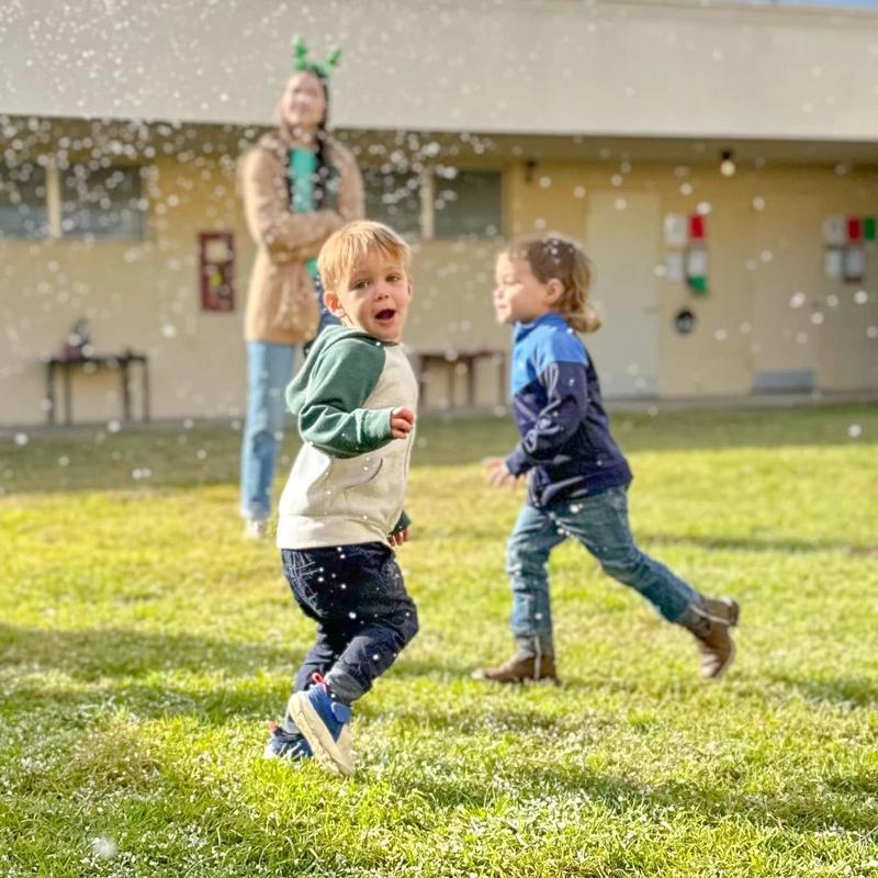 Two toddlers run through falling snow