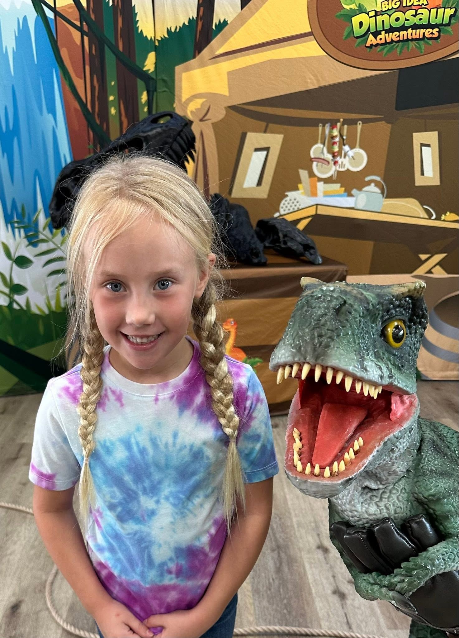A girl in a tie-dye shirt smiles next to a lifelike baby T. rex