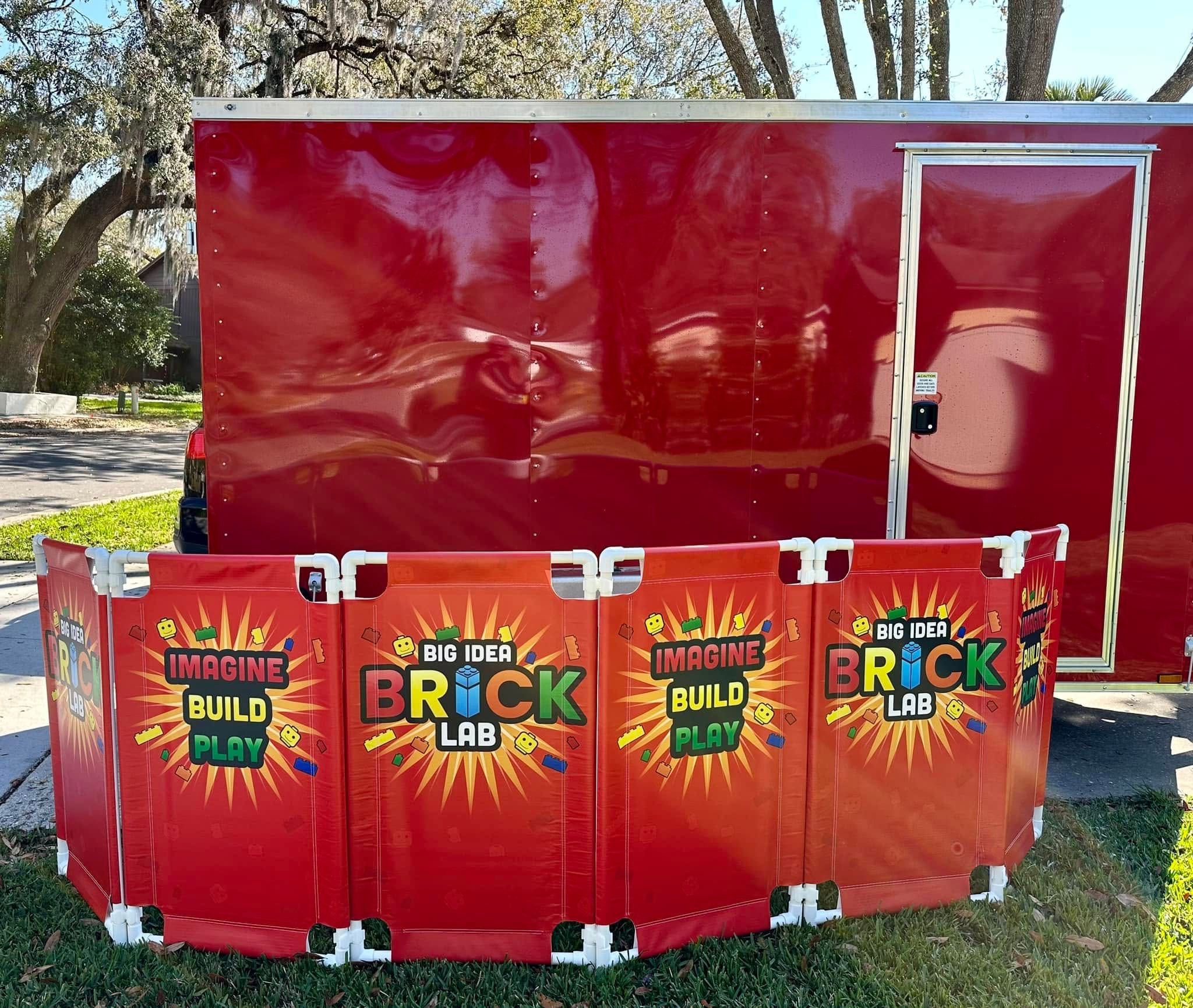 Brick Lab and Imagine Build Play panels set up on the grass in front of the red trailer