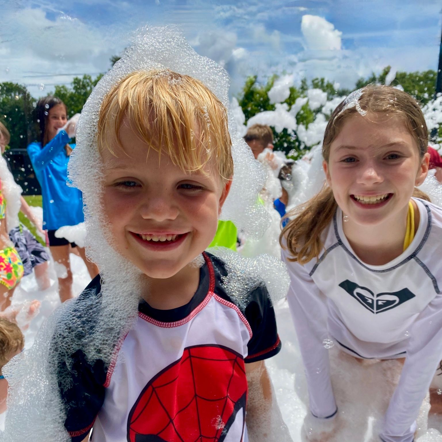 Kids laughing and diving into a mountain of fluffy white foam at a Foam Palooza party
