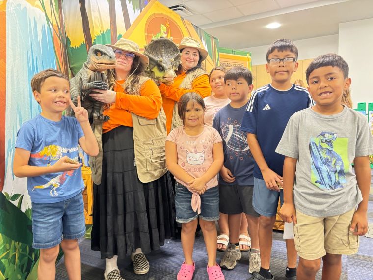 Two Dinosaur Trainers hold a baby triceratops and a baby velociraptor beside a group of kids