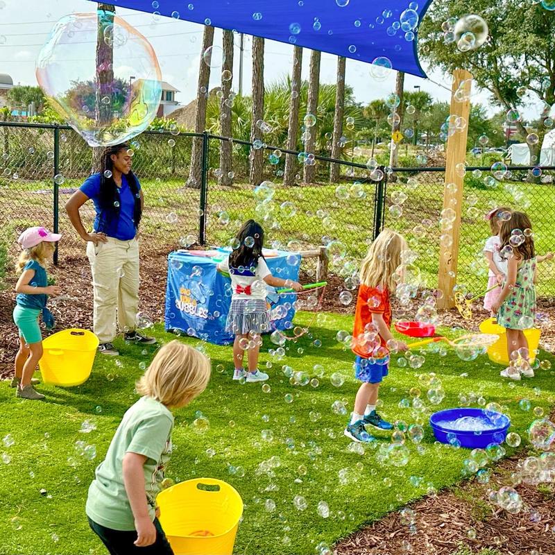 kids and a host making bubbles from blue buckets under a shade sail on a playground