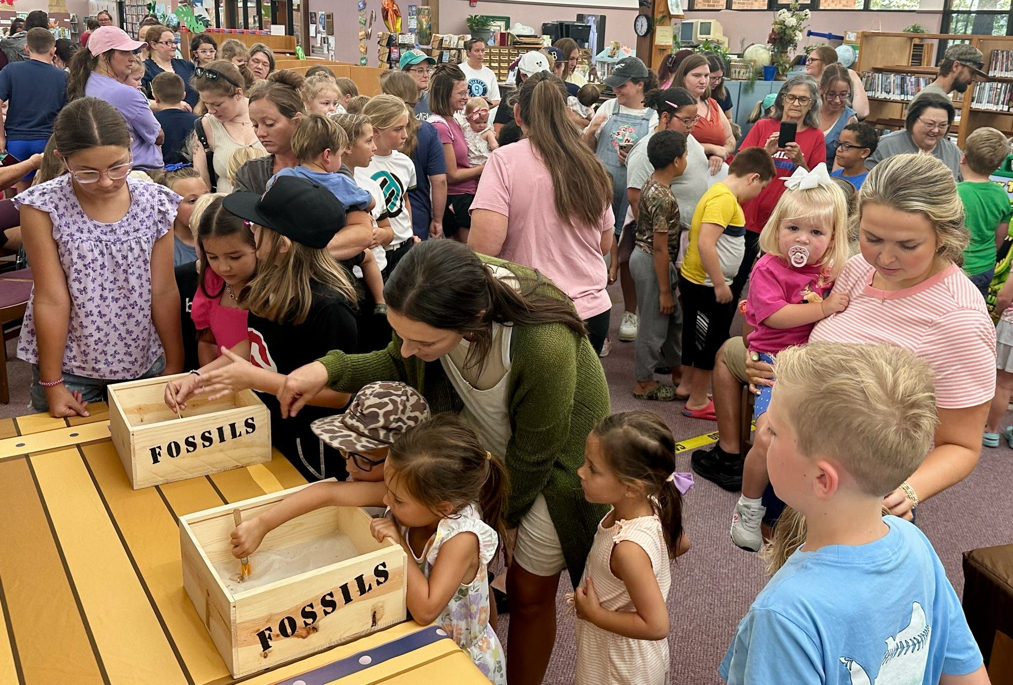 A crowd of kids and parents digs for fossils along a row of dig boxes