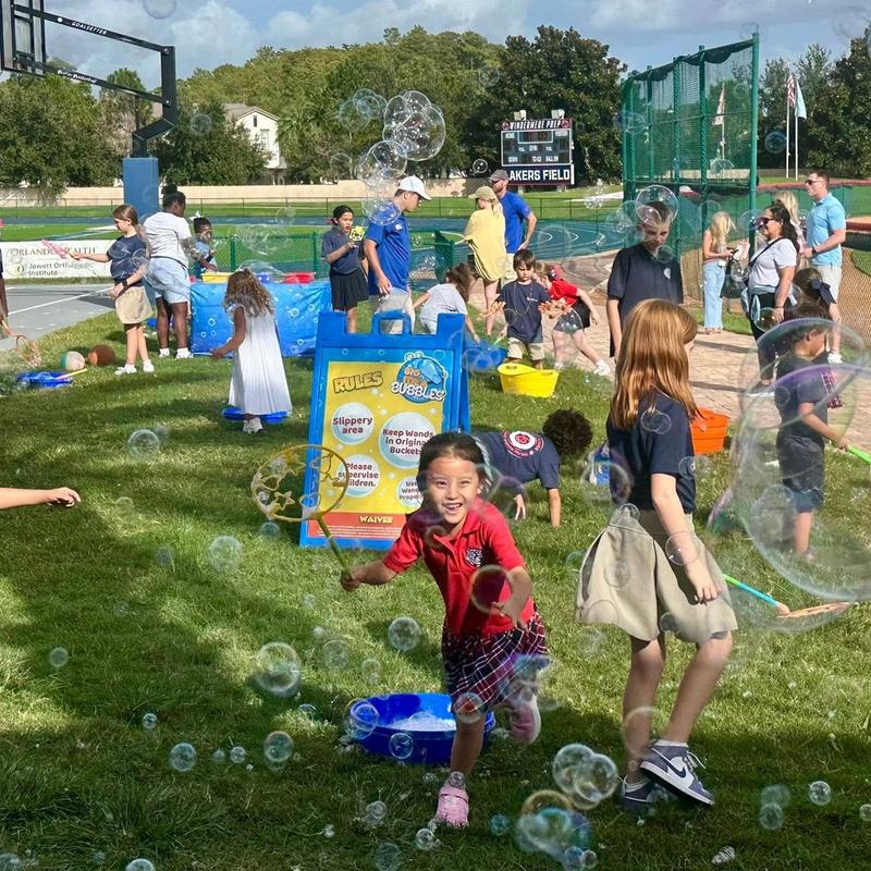 a crowd of kids making giant bubbles beside a Big Idea Bubbles sign at a school field