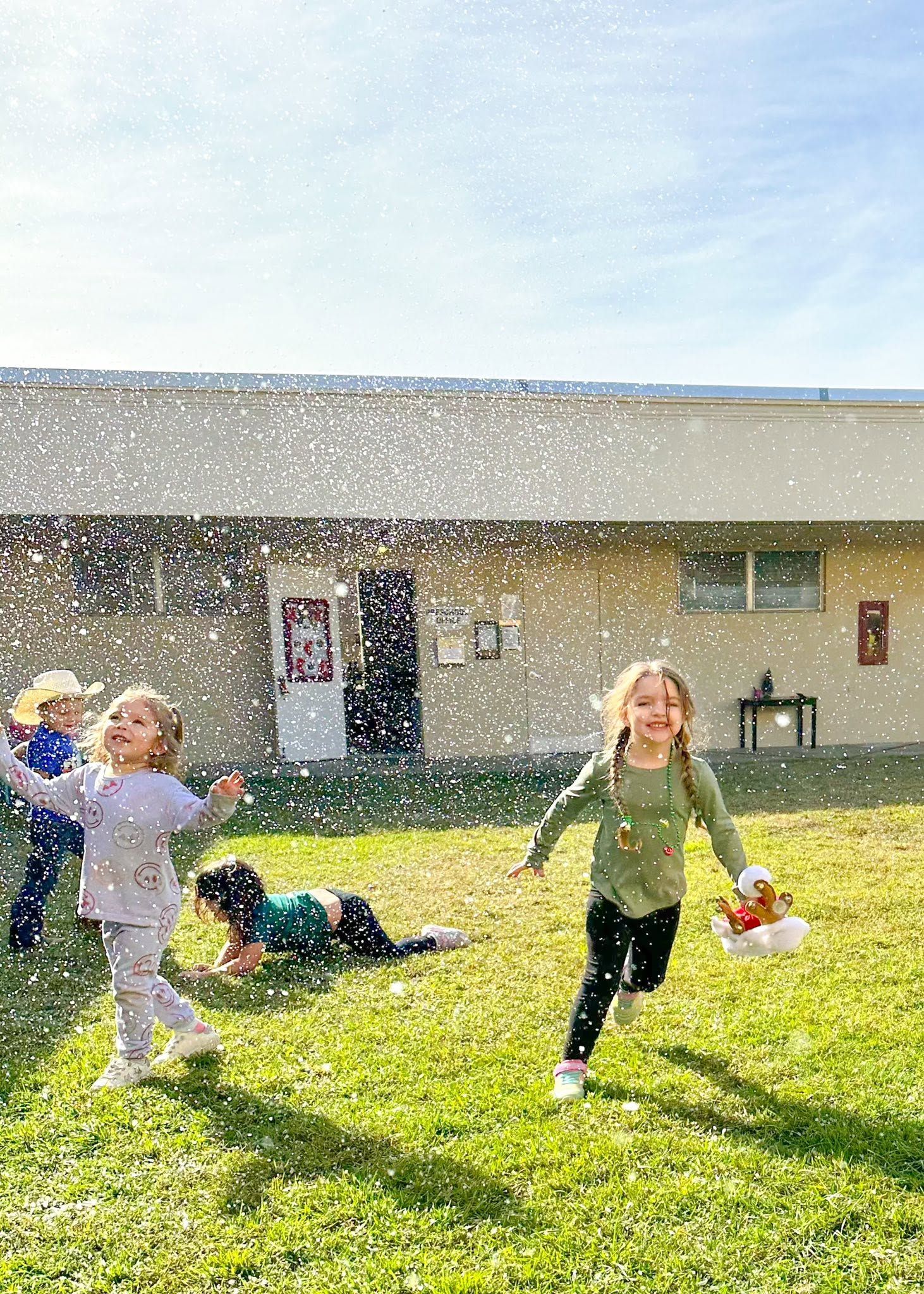 Young kids run and laugh across the grass as snow falls around them