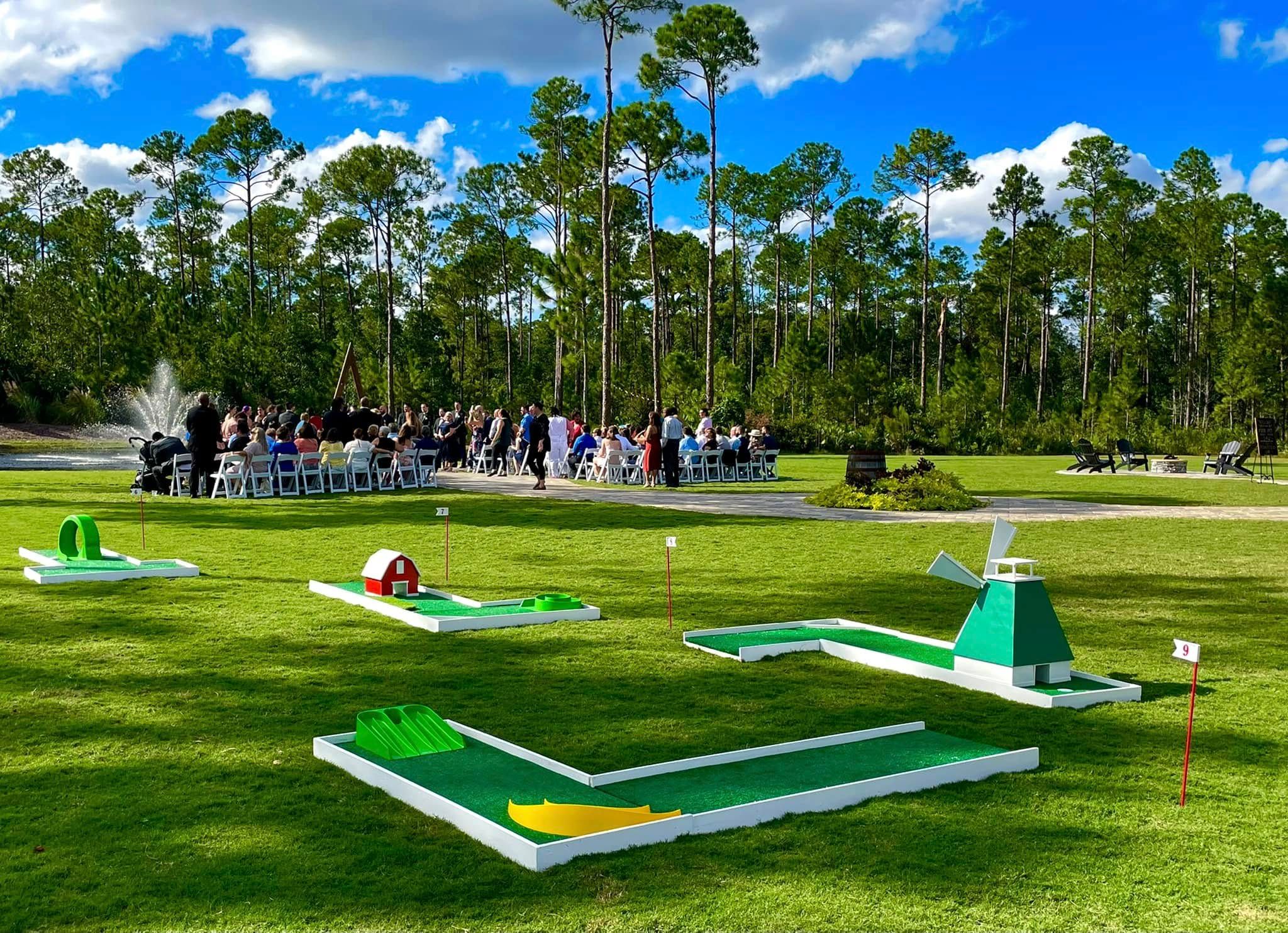 a row of portable mini golf holes on an open field with a crowd seated behind